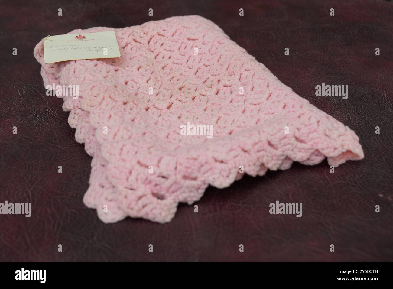 Eine pinkfarbene Babydecke, die vor fast 100 Jahren von Queen Mary bei Hansons Auctioneers in Etwall, Derbyshire, hergestellt wurde, bevor sie am Freitag zur Auktion aufsteigt. Die von Queen Mary gefertigte Häkeldecke trägt noch immer das Etikett „Made by her Majesty the Queen“ im Buckingham Palace. Sie wurde von der Verkäuferin im Haus ihrer 93-jährigen Tante in Wimbledon, Süd-London, entdeckt, aber keiner weiß, woher sie kam. Bilddatum: Mittwoch, 25. September 2024. Stockfoto