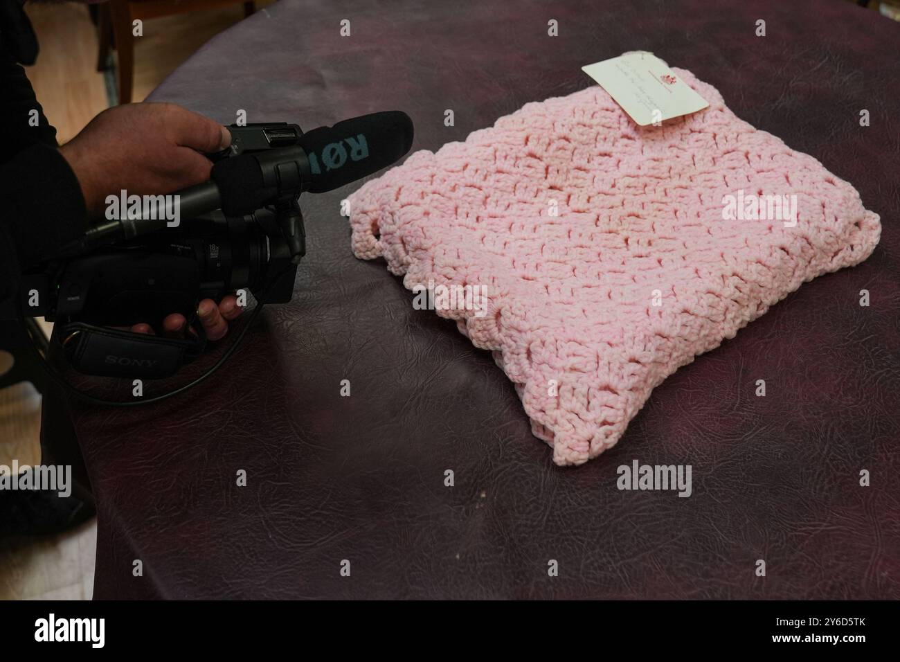 Eine pinkfarbene Babydecke, die vor fast 100 Jahren von Queen Mary bei Hansons Auctioneers in Etwall, Derbyshire, hergestellt wurde, bevor sie am Freitag zur Auktion aufsteigt. Die von Queen Mary gefertigte Häkeldecke trägt noch immer das Etikett „Made by her Majesty the Queen“ im Buckingham Palace. Sie wurde von der Verkäuferin im Haus ihrer 93-jährigen Tante in Wimbledon, Süd-London, entdeckt, aber keiner weiß, woher sie kam. Bilddatum: Mittwoch, 25. September 2024. Stockfoto