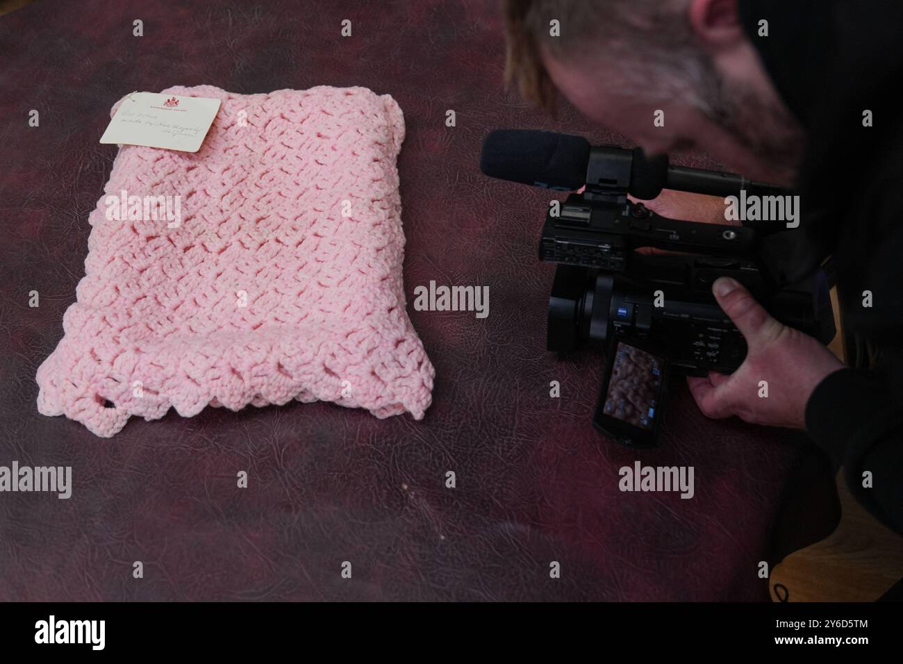 Eine pinkfarbene Babydecke, die vor fast 100 Jahren von Queen Mary bei Hansons Auctioneers in Etwall, Derbyshire, hergestellt wurde, bevor sie am Freitag zur Auktion aufsteigt. Die von Queen Mary gefertigte Häkeldecke trägt noch immer das Etikett „Made by her Majesty the Queen“ im Buckingham Palace. Sie wurde von der Verkäuferin im Haus ihrer 93-jährigen Tante in Wimbledon, Süd-London, entdeckt, aber keiner weiß, woher sie kam. Bilddatum: Mittwoch, 25. September 2024. Stockfoto