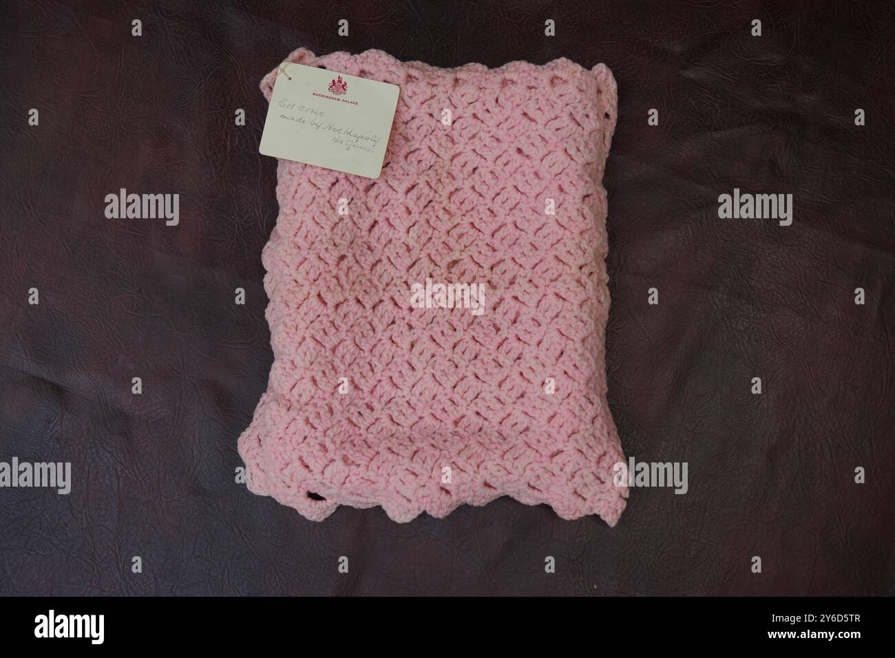 Eine pinkfarbene Babydecke, die vor fast 100 Jahren von Queen Mary bei Hansons Auctioneers in Etwall, Derbyshire, hergestellt wurde, bevor sie am Freitag zur Auktion aufsteigt. Die von Queen Mary gefertigte Häkeldecke trägt noch immer das Etikett „Made by her Majesty the Queen“ im Buckingham Palace. Sie wurde von der Verkäuferin im Haus ihrer 93-jährigen Tante in Wimbledon, Süd-London, entdeckt, aber keiner weiß, woher sie kam. Bilddatum: Mittwoch, 25. September 2024. Stockfoto
