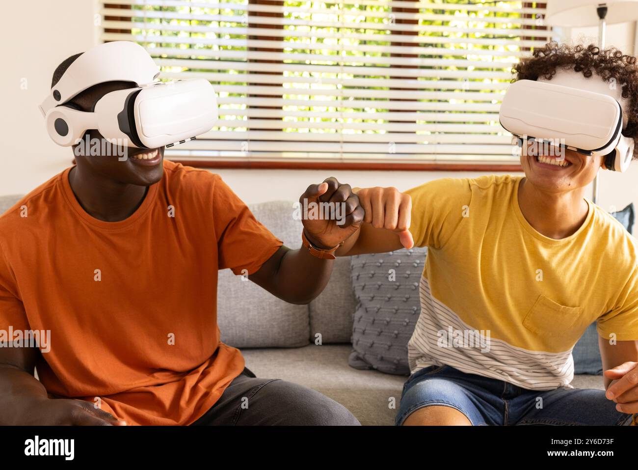 Zu Hause, mit VR-Headsets, schlagen zwei verschiedene männliche Freunde mit der Faust, während sie Virtual Reality g genießen Stockfoto
