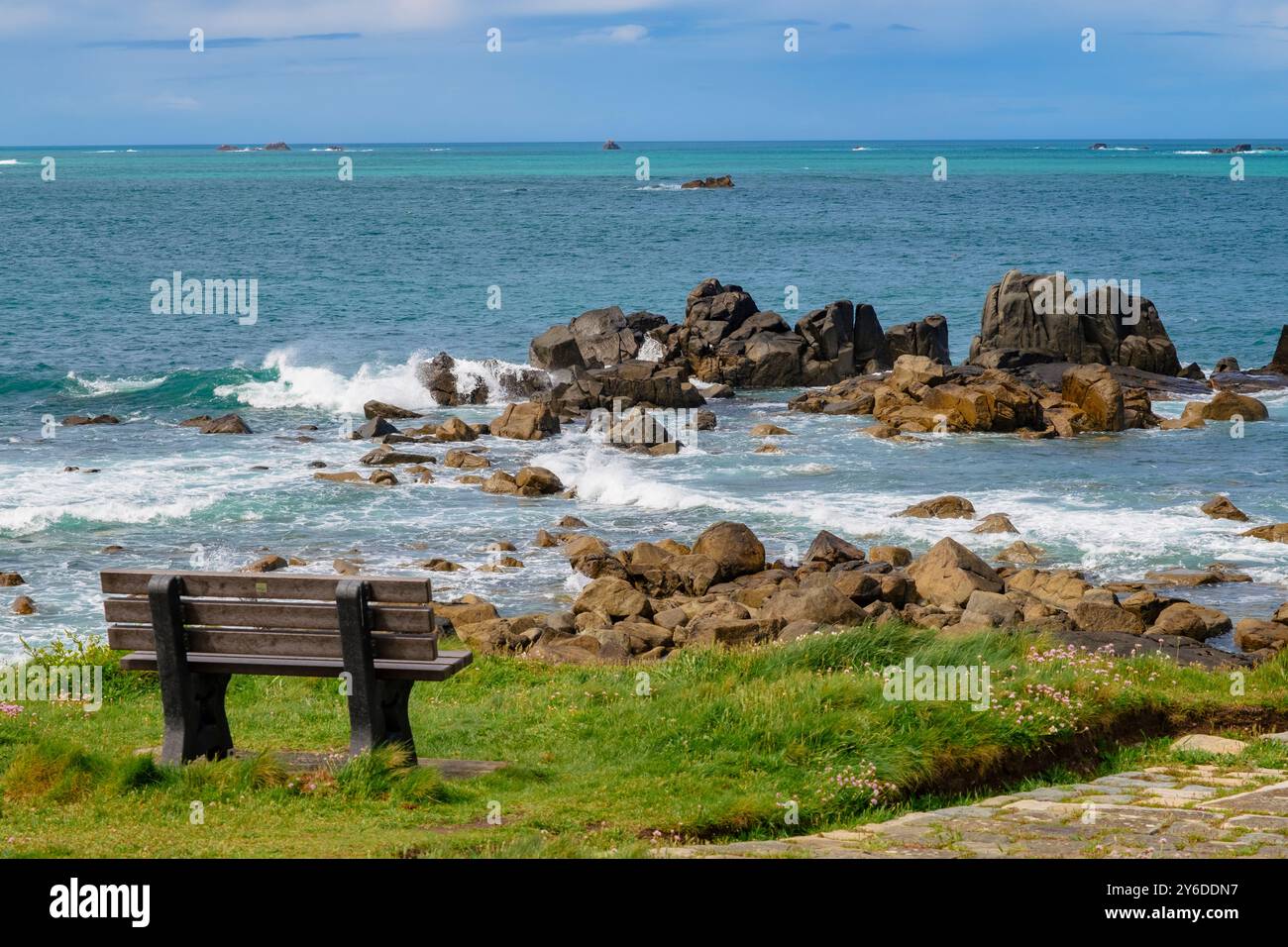 Grand Havre Bay und eine leere Bank am Küstenweg rund um Chouet Landzunge mit Wellen, die auf Felsen stürzen. Guernsey, Kanalinseln, Großbritannien Stockfoto