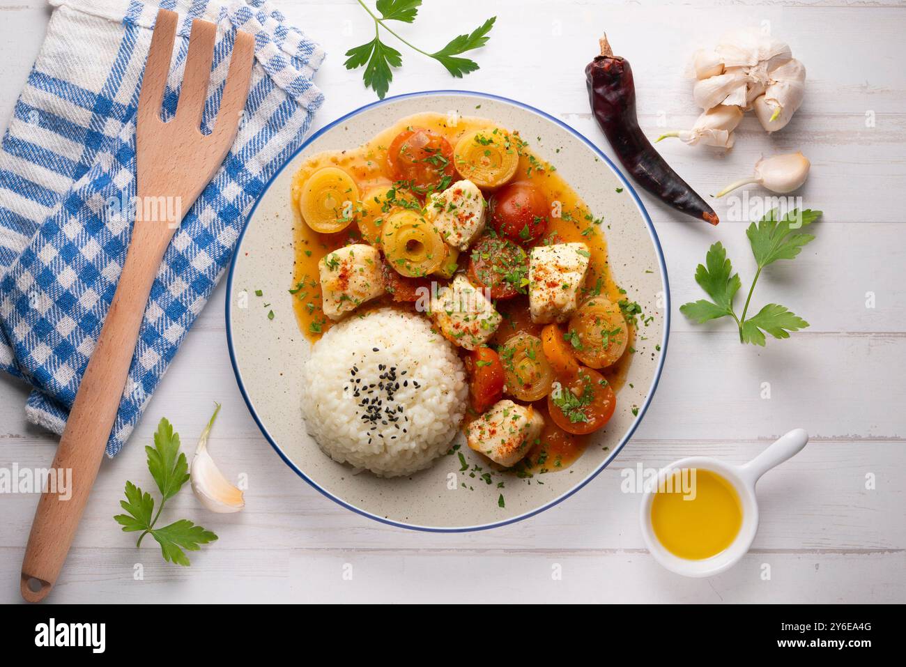 Weißfischeintopf mit Lauch und Kirschtomaten, serviert mit Reis. Tisch mit Draufsicht und Dekoration. Stockfoto