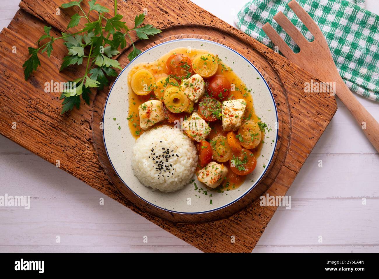 Weißfischeintopf mit Lauch und Kirschtomaten, serviert mit Reis. Tisch mit Draufsicht und Dekoration. Stockfoto