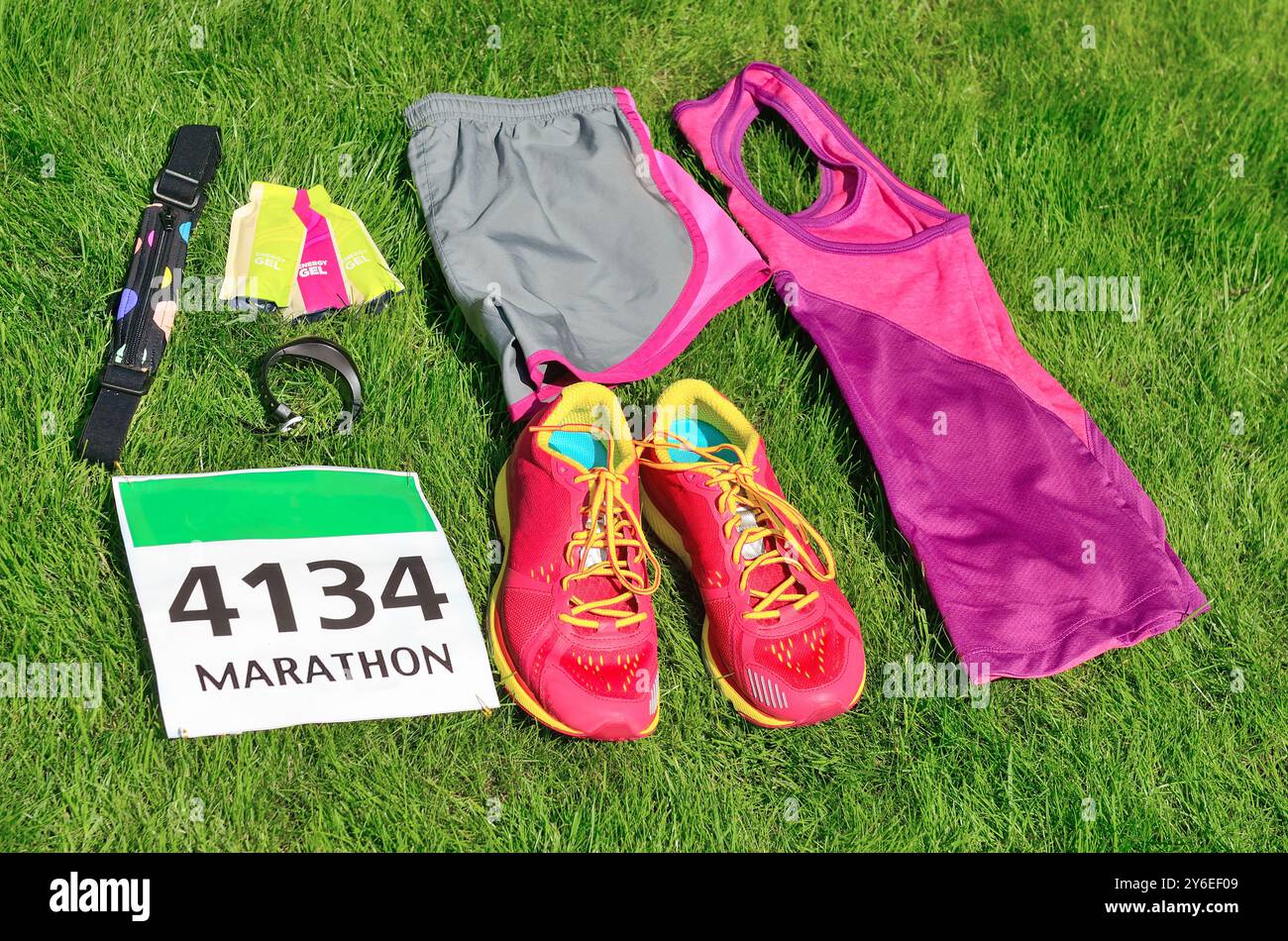 Laufschuhe, Marathon-Race-Lätzchen (Anzahl), Laufausrüstung und Energiegels auf Grashintergrund, Sportwettbewerb, Fitness und gesundes Lifestyle-Konzept Stockfoto