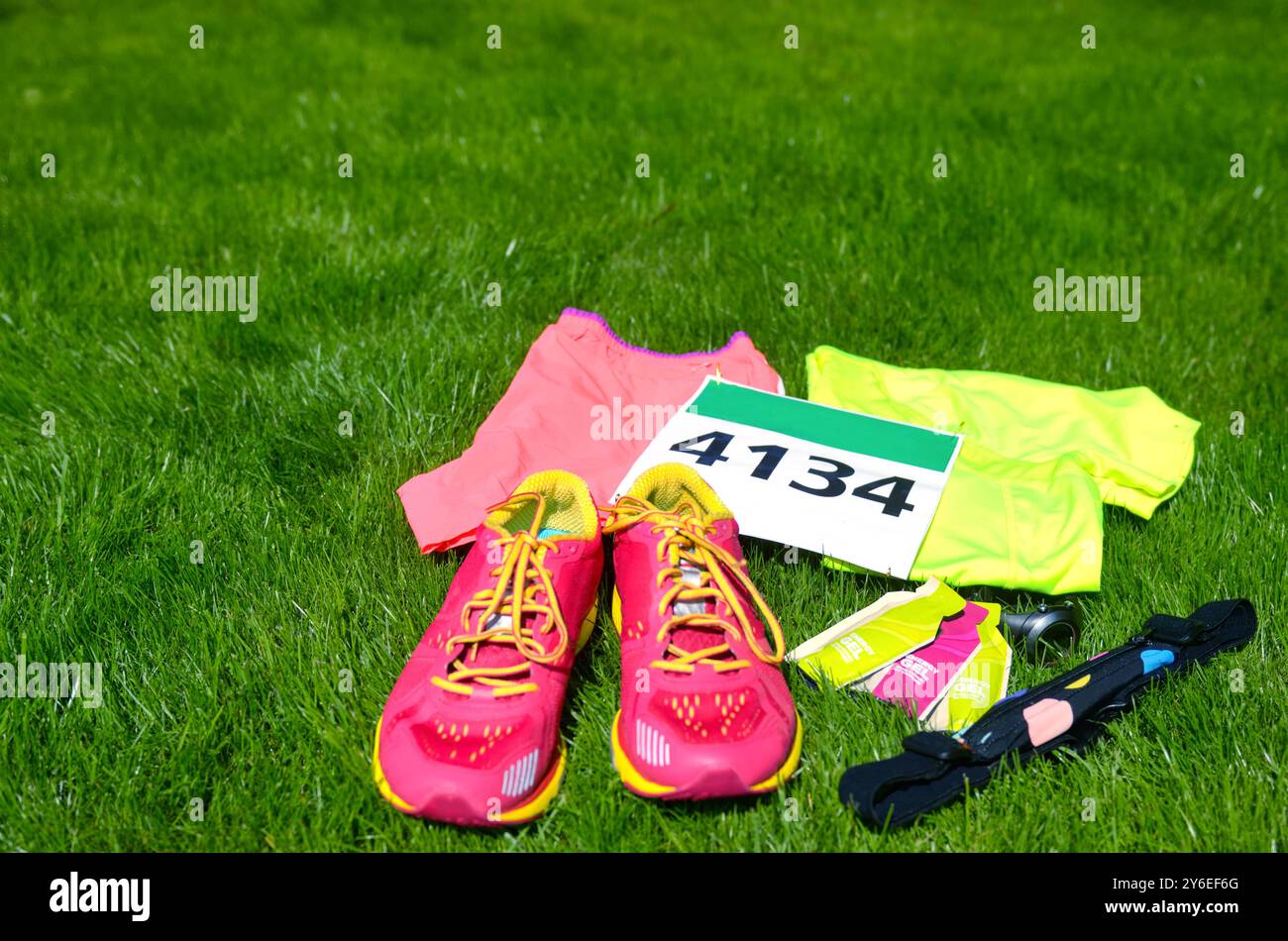 Laufschuhe, Marathon-Race-Lätzchen (Anzahl), Laufausrüstung und Energiegels auf Grashintergrund, Sportwettbewerb, Fitness und gesundes Lifestyle-Konzept Stockfoto