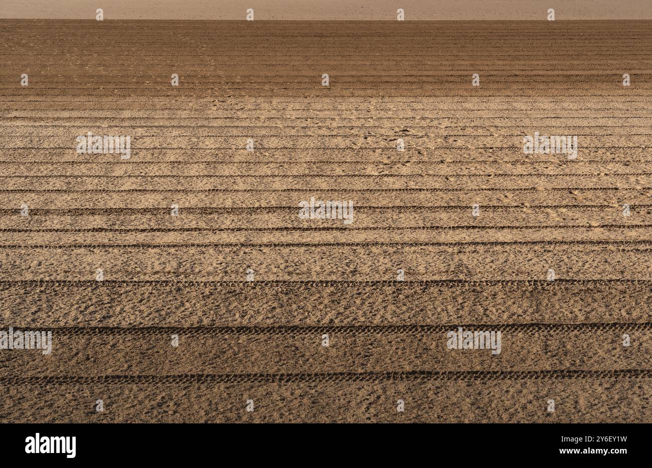 Nahaufnahme von gemustertem Sand mit parallelen Linien und Texturen, die durch Reifenspuren erzeugt werden. Stockfoto