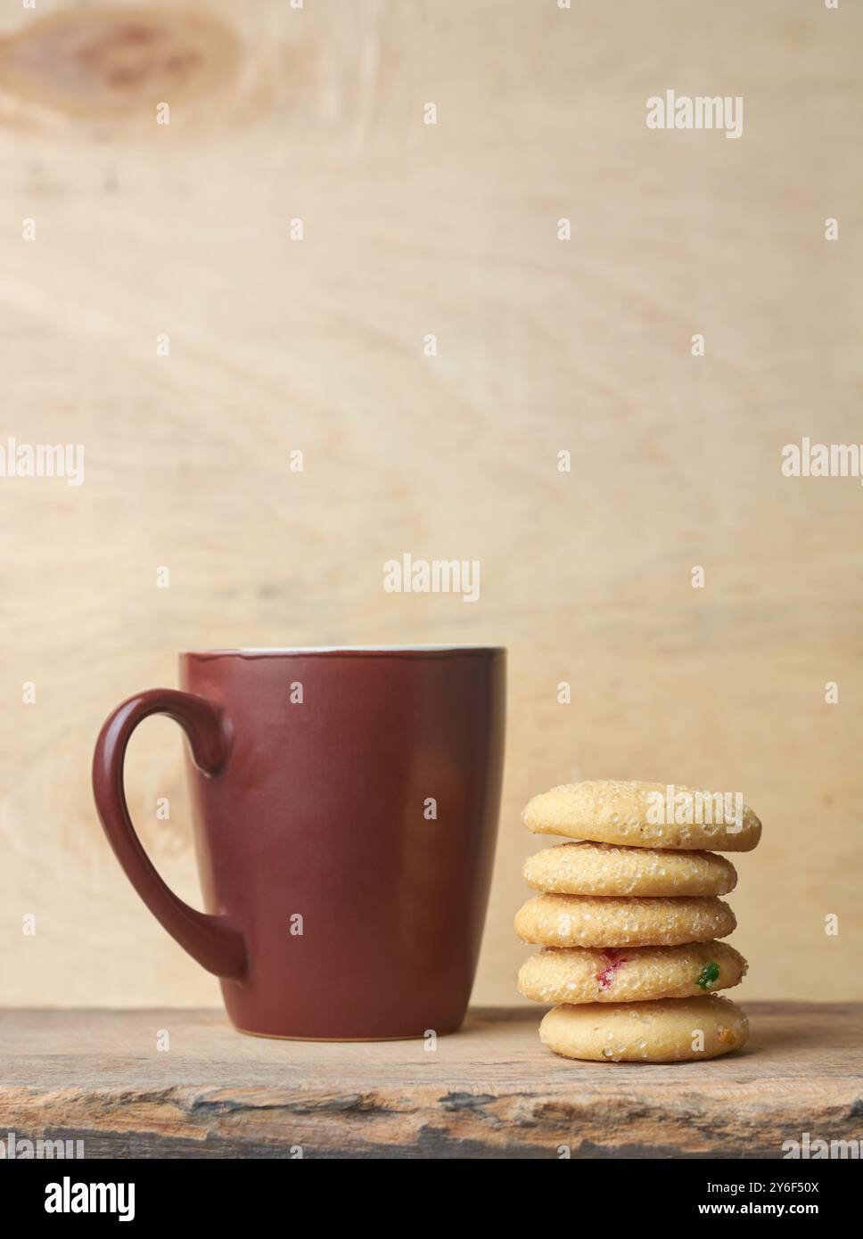 Gestapelte Zuckerkekse auf Holztisch mit Tasse oder Becher im Hintergrund, gebackene süße Kekse mit knackiger Textur und Buttergeschmack, Kopierraum Stockfoto