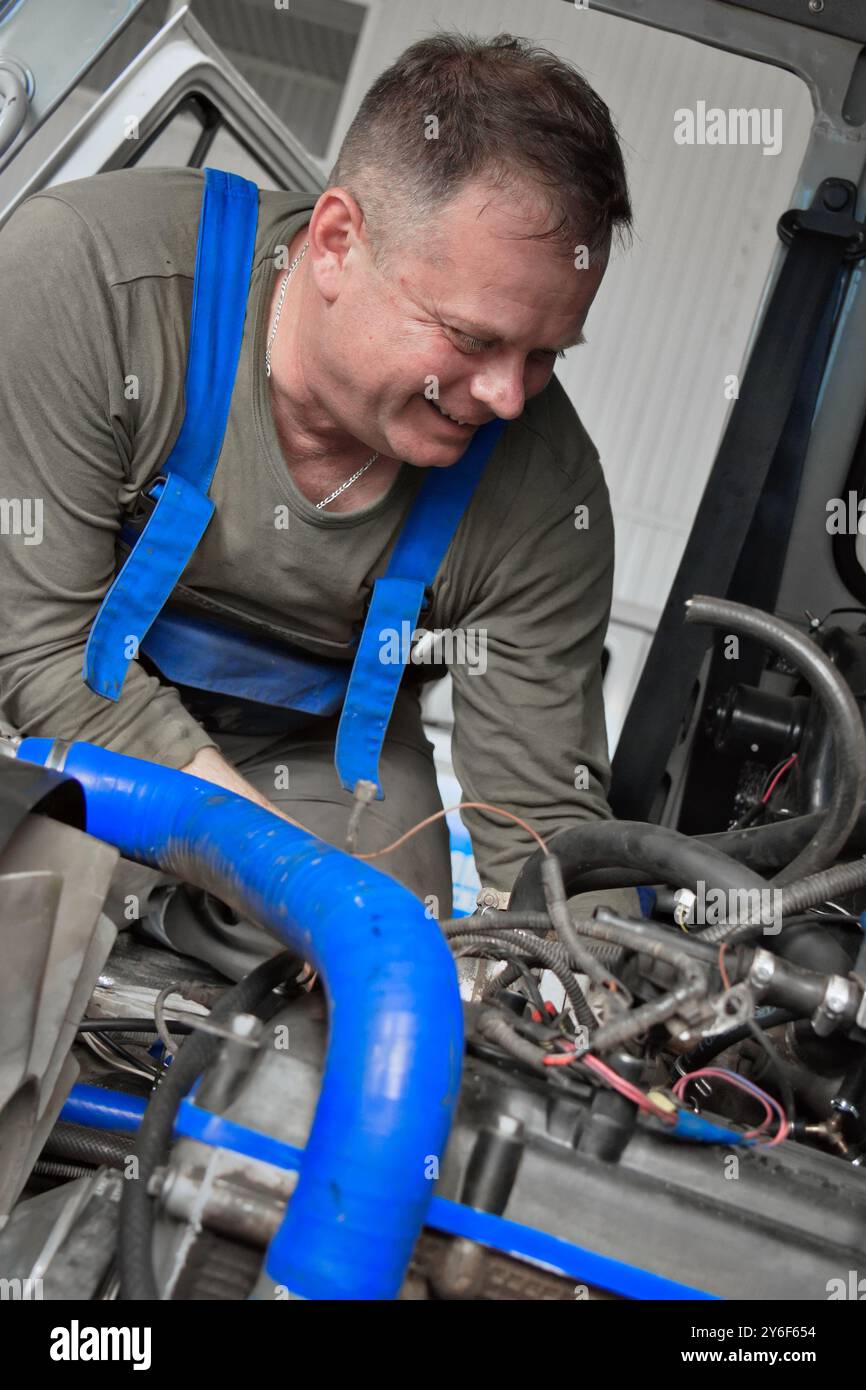 Ein Mechaniker inspiziert und repariert Motorkomponenten in einer Garage sorgfältig und demonstriert sein Fachwissen und seine Liebe zum Detail. In praktischer Kleidung bedient er verschiedene Werkzeuge, während er von anspruchsvoller Technologie umgeben ist. Stockfoto