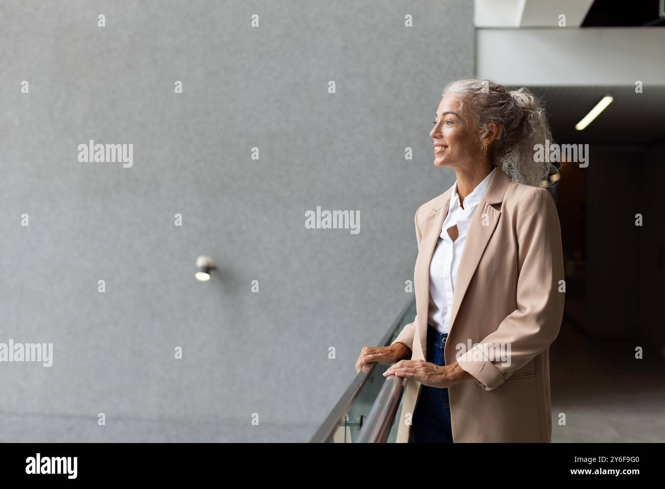Lächelnde Frau in Geschäftskleidung, die am Geländer steht, in die Ferne schaut, Kopierraum Stockfoto
