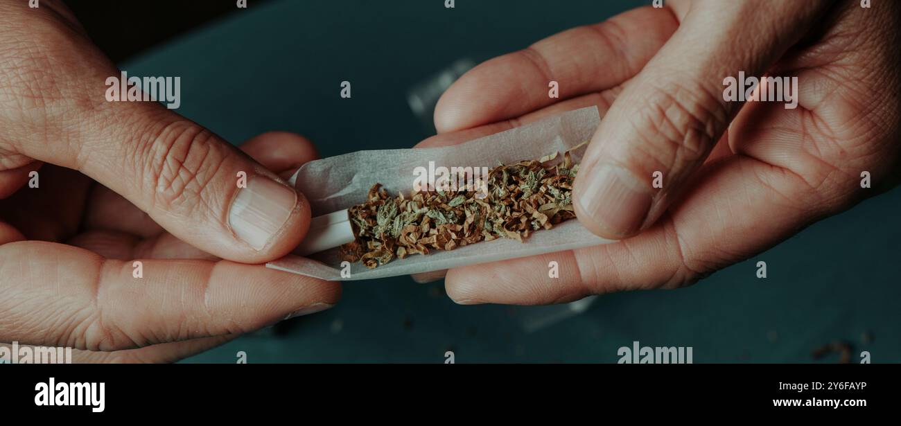 Nahaufnahme eines Mannes, der gerade einen Joint Rollen wird, hergestellt aus Cannabis gemischt mit Tabak, in einem Panoramaformat, um ihn als Webbanner zu verwenden Stockfoto