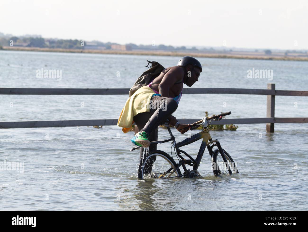 Ein Mann wird versuchen, sein Fahrrad zu fahren, das im tiefen Wasser auf einer überfluteten Straße steht. Stockfoto