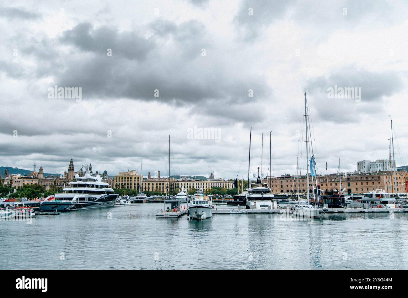 Malerischer Blick auf den Hafen von Port Vell in Barcelona mit Luxusyachten, historischen Gebäuden und einem bewölkten Himmel, der die malerische Uferpromenade der Stadt erfasst Stockfoto