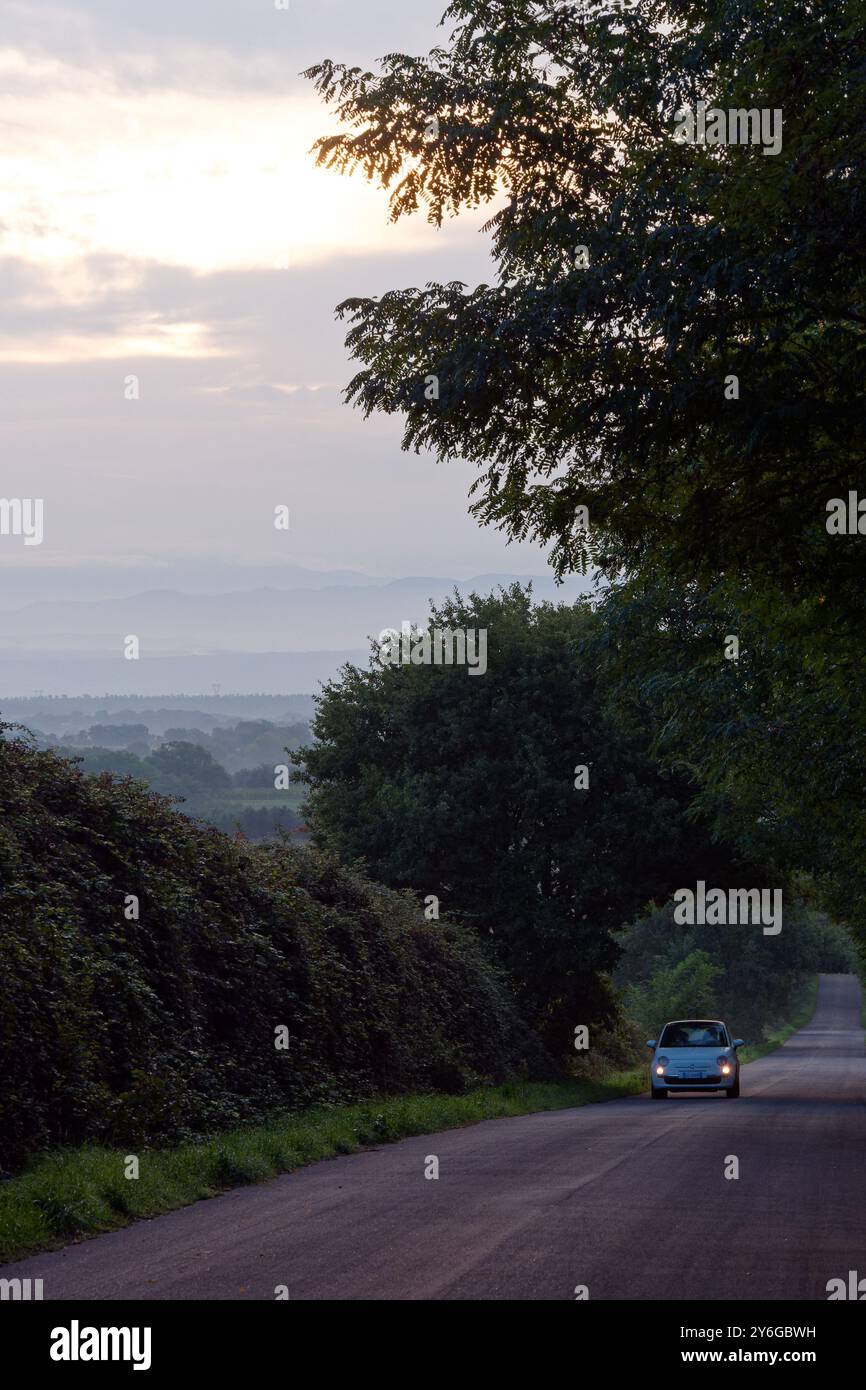 Auto mit Scheinwerfern an, auf einer Landstraße mit Blick auf die Berge eines morgens in der Stadt Montefiascone, Region Latium, Italien. September 2024. Stockfoto