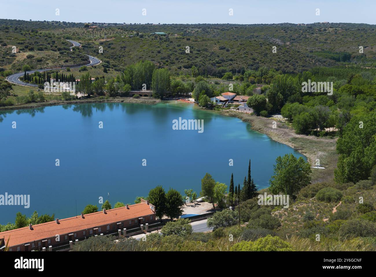 Blick auf einen ruhigen See mit umliegenden Häusern, Bäumen und Hügeln unter blauem Himmel, Blick von der Aussichtsplattform, Mirador de la Laguna del Rey, Lagun Stockfoto