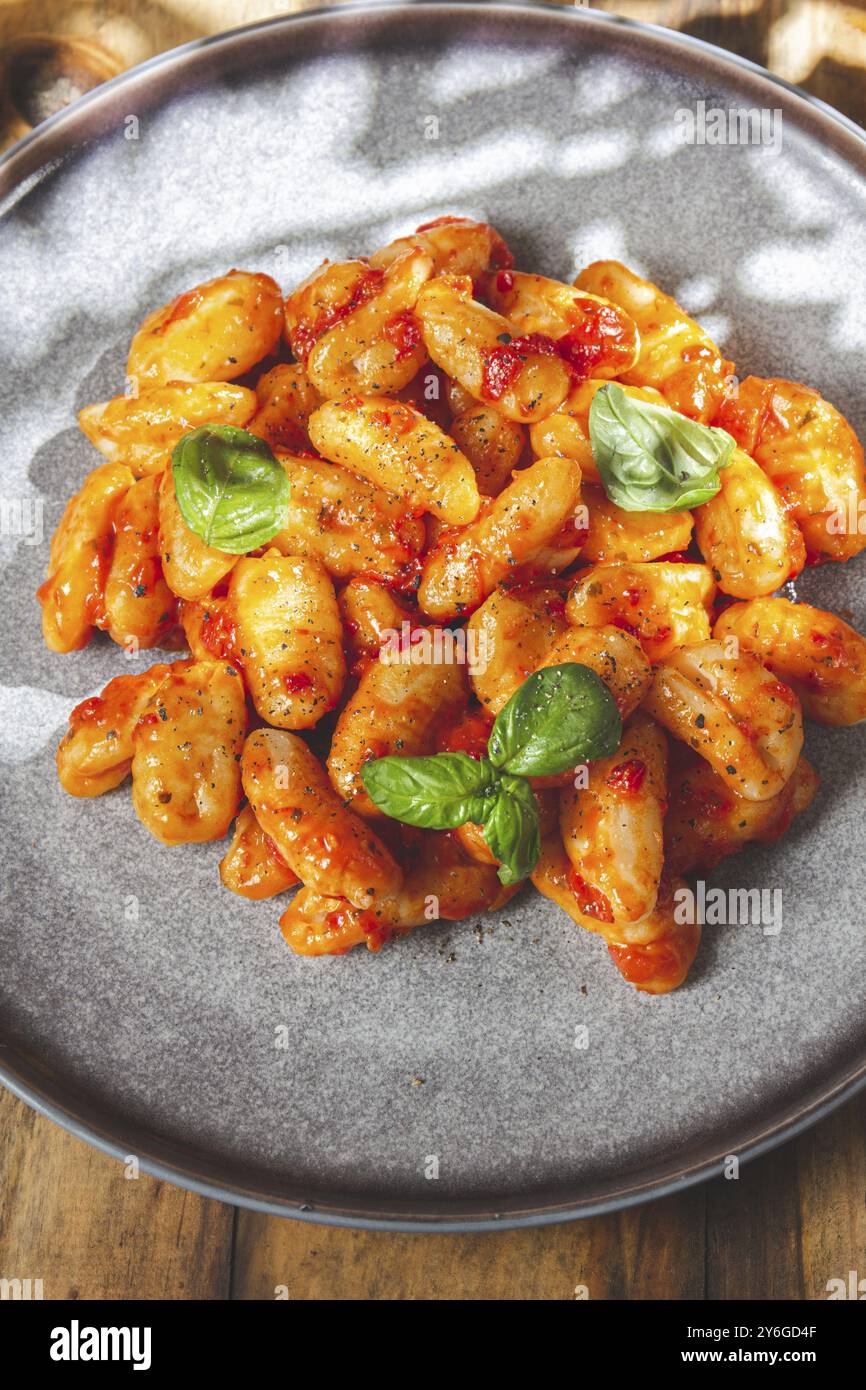 Lebensmittelfotografie, Nahaufnahme von italienischen Kartoffel-Gnocchi mit Tomatensauce und frischem Basilikum auf grauer Platte auf hölzernem Hintergrund Stockfoto