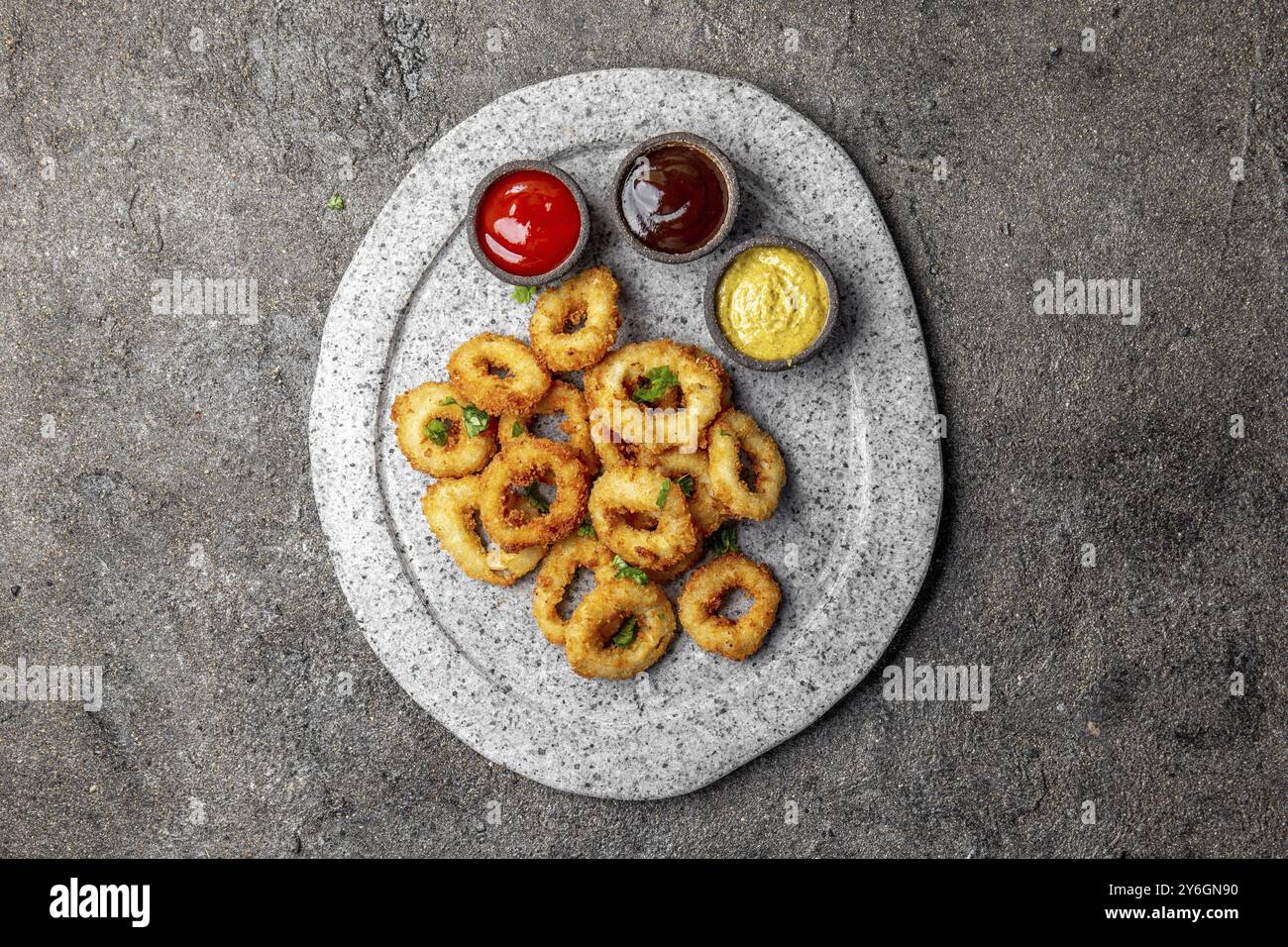 Essen, Essen, gebratene Tintenfische Ringe auf grauem Steinteller mit Saucen. Grauer Betonhintergrund Stockfoto