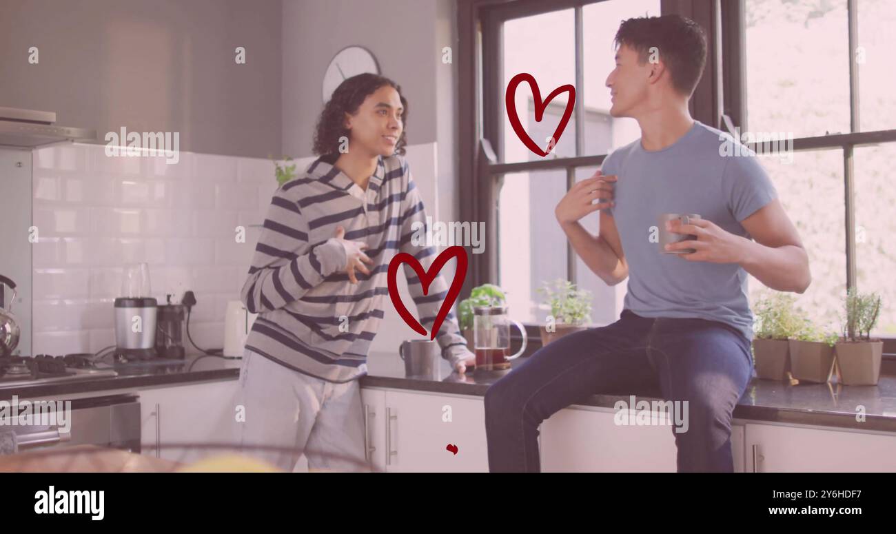Bild von roten Herzen über glückliche, verschiedene schwule männliche Paare, die in der Küche reden und lachen Stockfoto