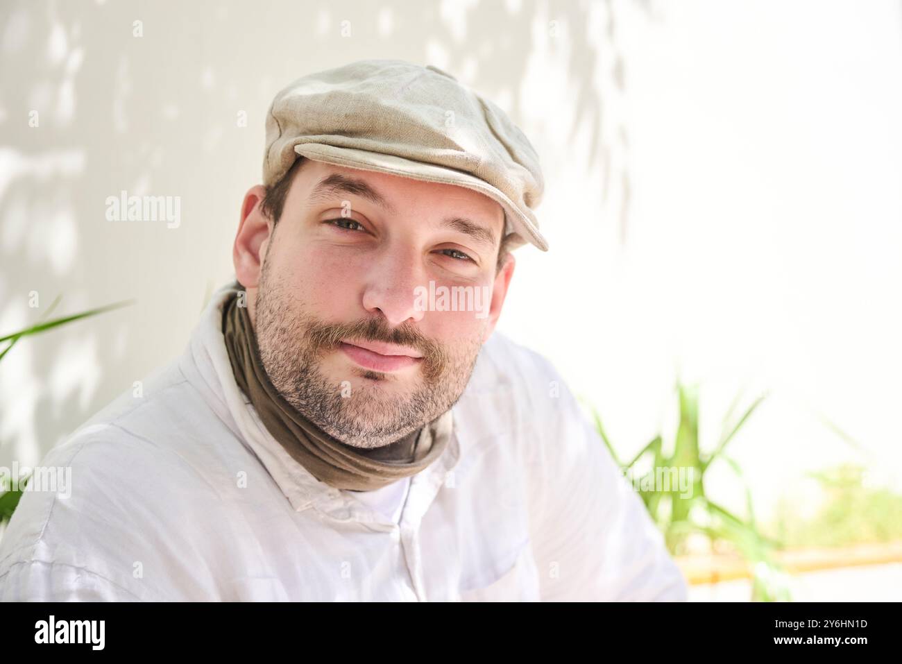 Nahaufnahme Porträt eines jungen Mannes, der in einem sonnigen Innenhof sitzt und lächelnd in die Kamera blickt. Die Szene ist hell und vermittelt ein Gefühl von Nähe Stockfoto