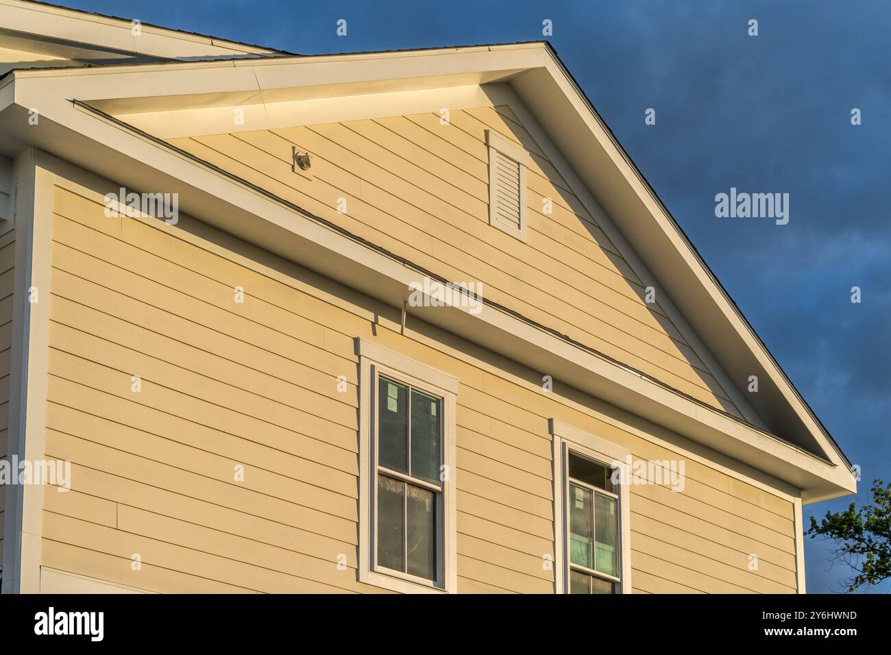 Sun malte die Seite eines amerikanischen Neubauhauses mit gelbem traditionellen Lap-Vinyl-Abstellgleis, gelbem Fensterrahmen und Giebelgiebel gelb Stockfoto