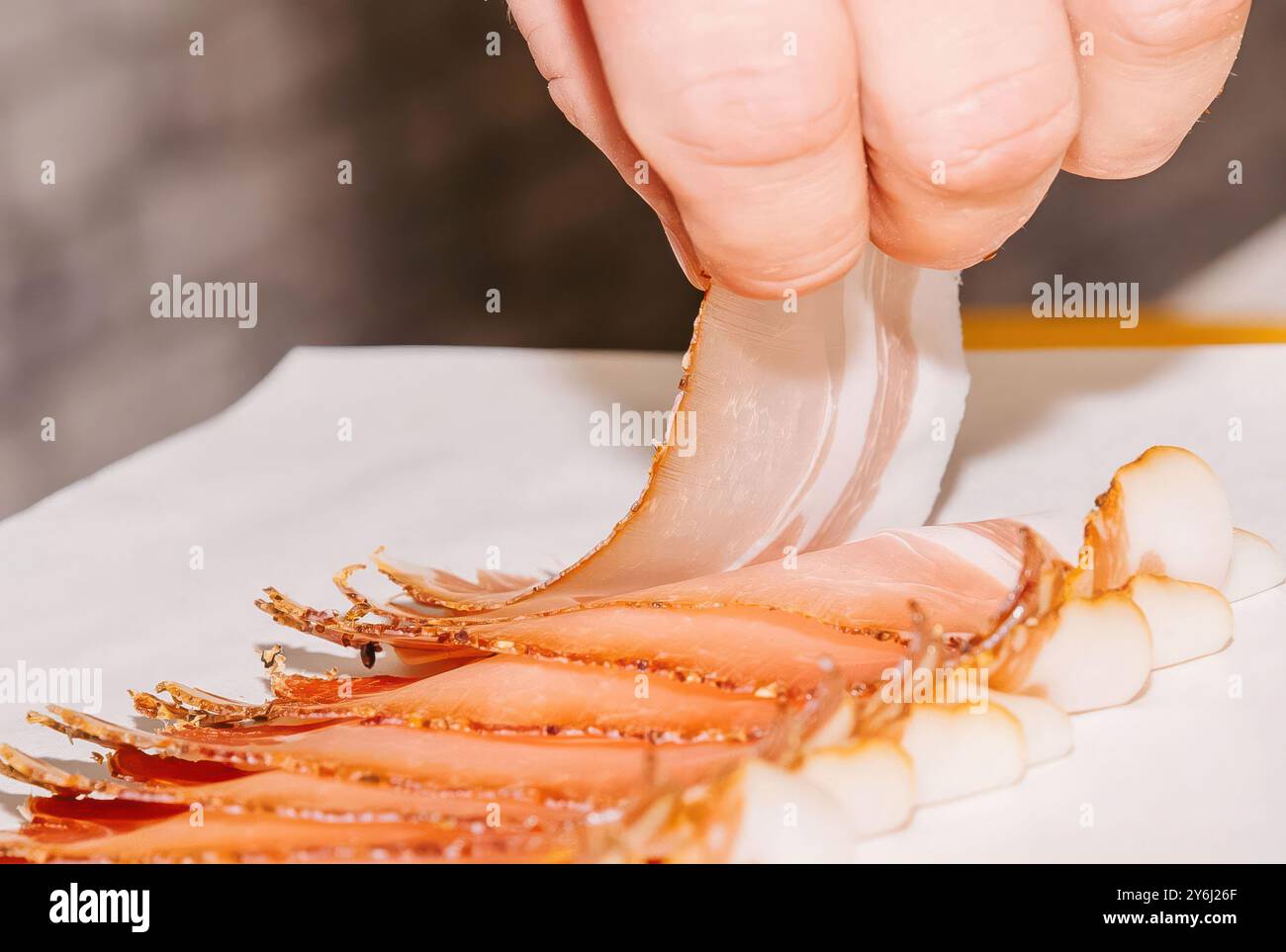 Zart mit dünn geschnittenem Schinken, Person auf weißem Pergament, kulinarisches Zubereitungskonzept Stockfoto