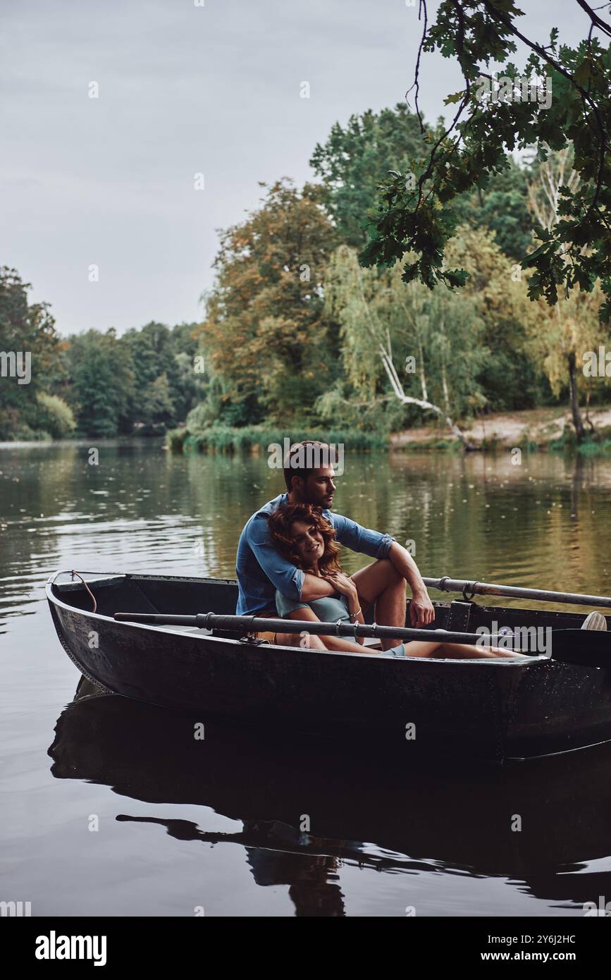 Sorgen hinter sich lassen. Wunderschönes junges Paar, das sich umschließt und lächelt, während es ein romantisches Date auf dem See genießt Stockfoto