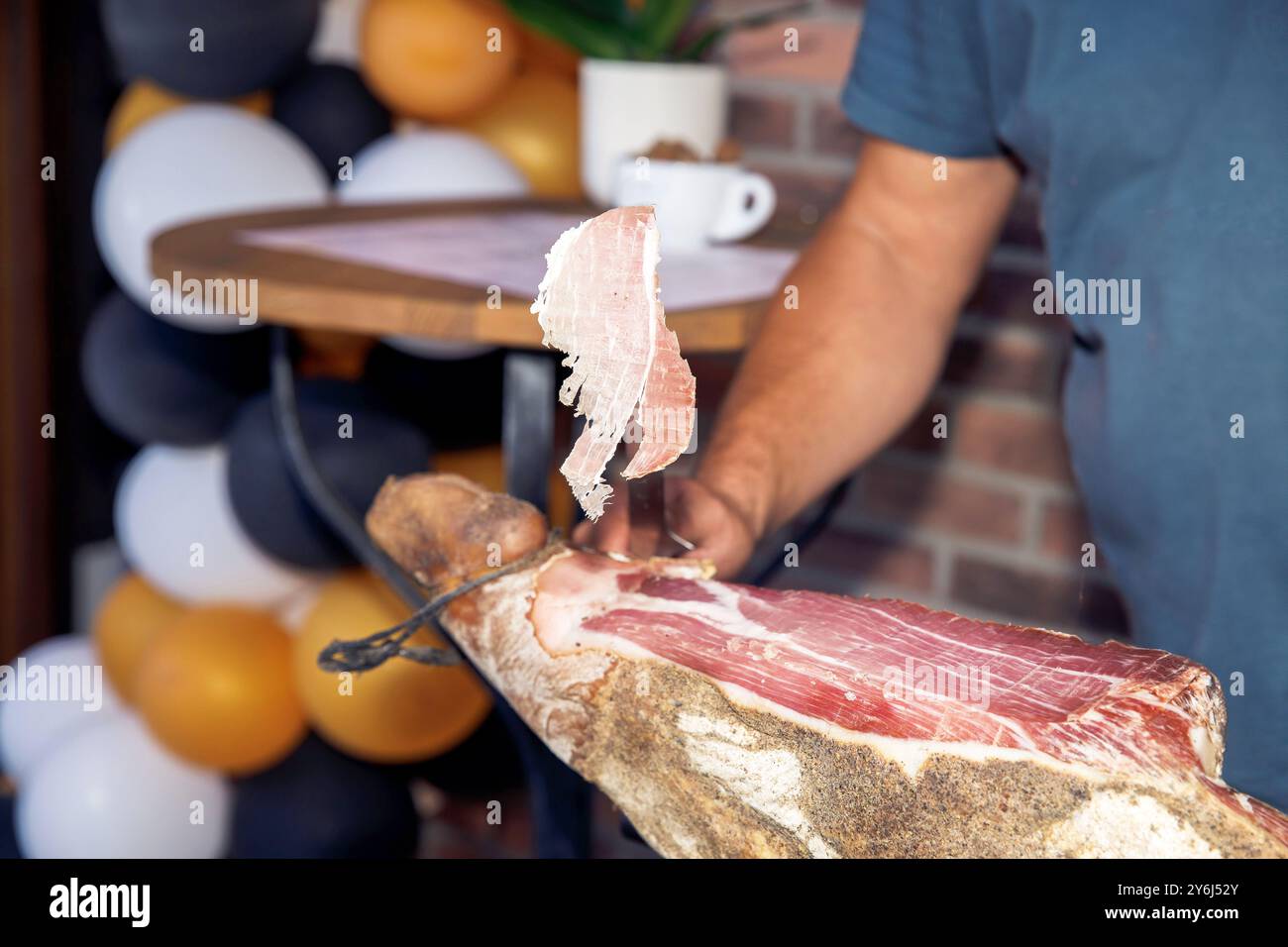 Person schneidet Schinken, in Scheiben geschnittenen Schinken, Küchentisch, kulinarische Zubereitung, kulinarisches Delikatessen-Konzept Stockfoto