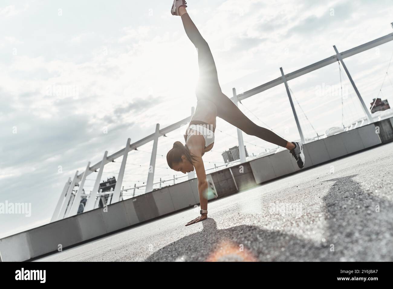 Welt auf den Kopf gestellt. Die ganze Länge einer modernen jungen Frau in Sportbekleidung, die beim Training im Freien Handstand macht Stockfoto