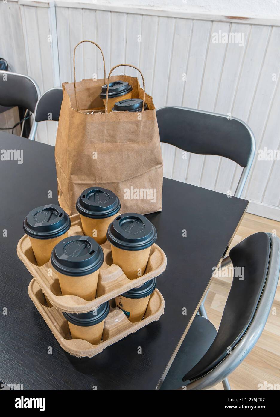 Ein Tisch mit einem Stapel Kaffeetassen und einer braunen Papiertüte. Der Tisch ist schwarz und befindet sich in einem Büro mit weißen Wänden. Stockfoto