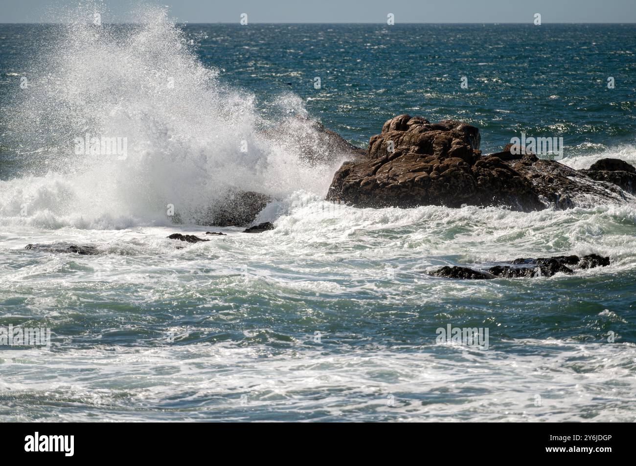 Mächtige Wellen krachen entlang der Küste auf Felsen und erzeugen einen nebeligen Sprühnebel. Stockfoto