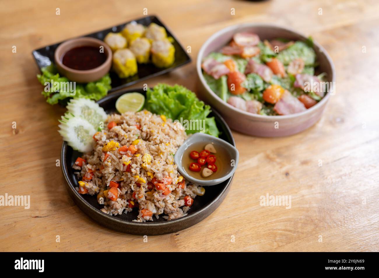 Ein hölzerner Esstisch in einem Restaurant oder zu Hause mit einem Teller gebratenem Reis, einer Salatschale und einem Teller mit gedämpften Knödeln. Der Begriff der Nahrung Stockfoto