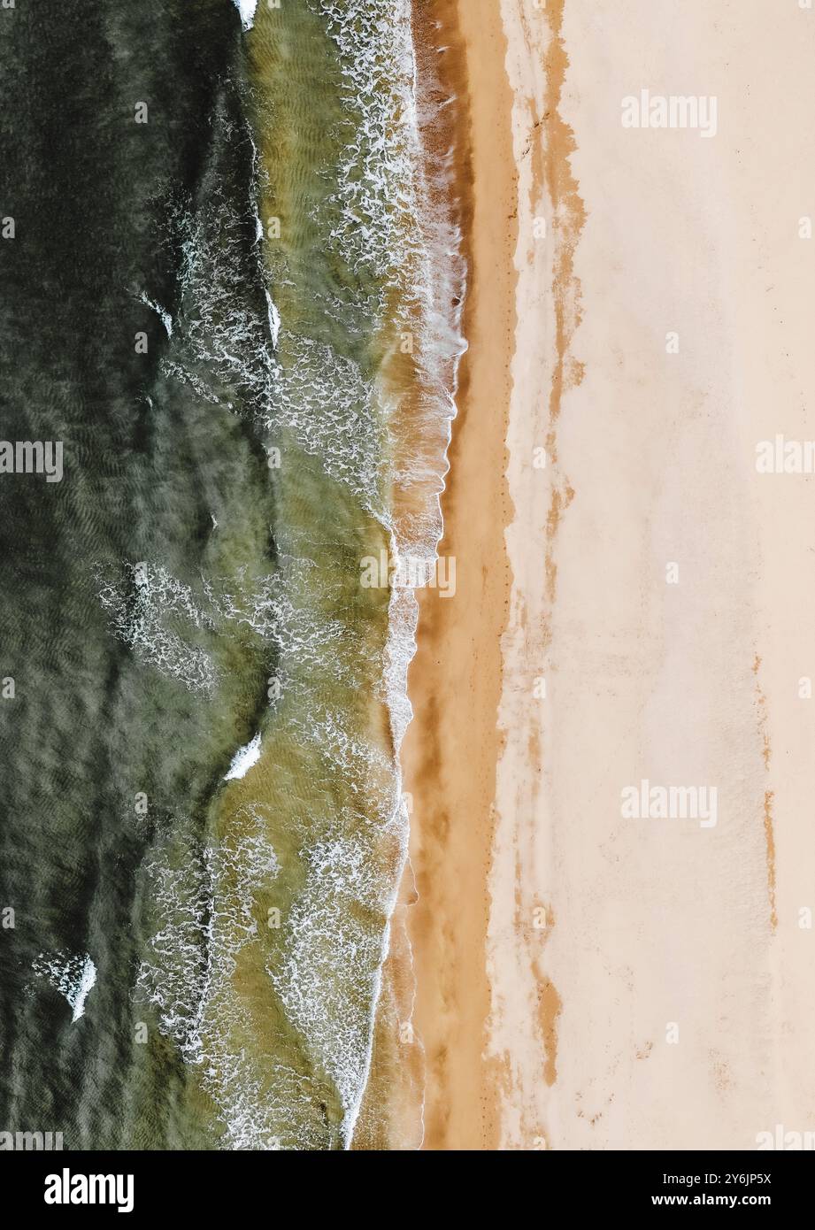 Aus der Vogelperspektive auf Meereswellen, die sanft auf einen Sandstrand gleiten, bilden einen wunderschönen Kontrast zwischen dem Wasser und dem Ufer. Stockfoto