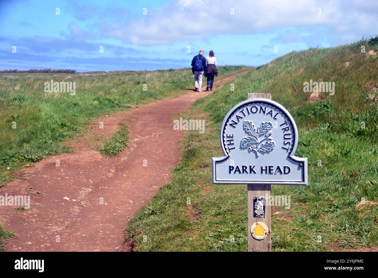 Paare gehen am National Trust Sign on the Path to Park Head in der Nähe von Porthcothan auf dem Southwest Coastal Path, North Cornwall, England, Großbritannien. Stockfoto