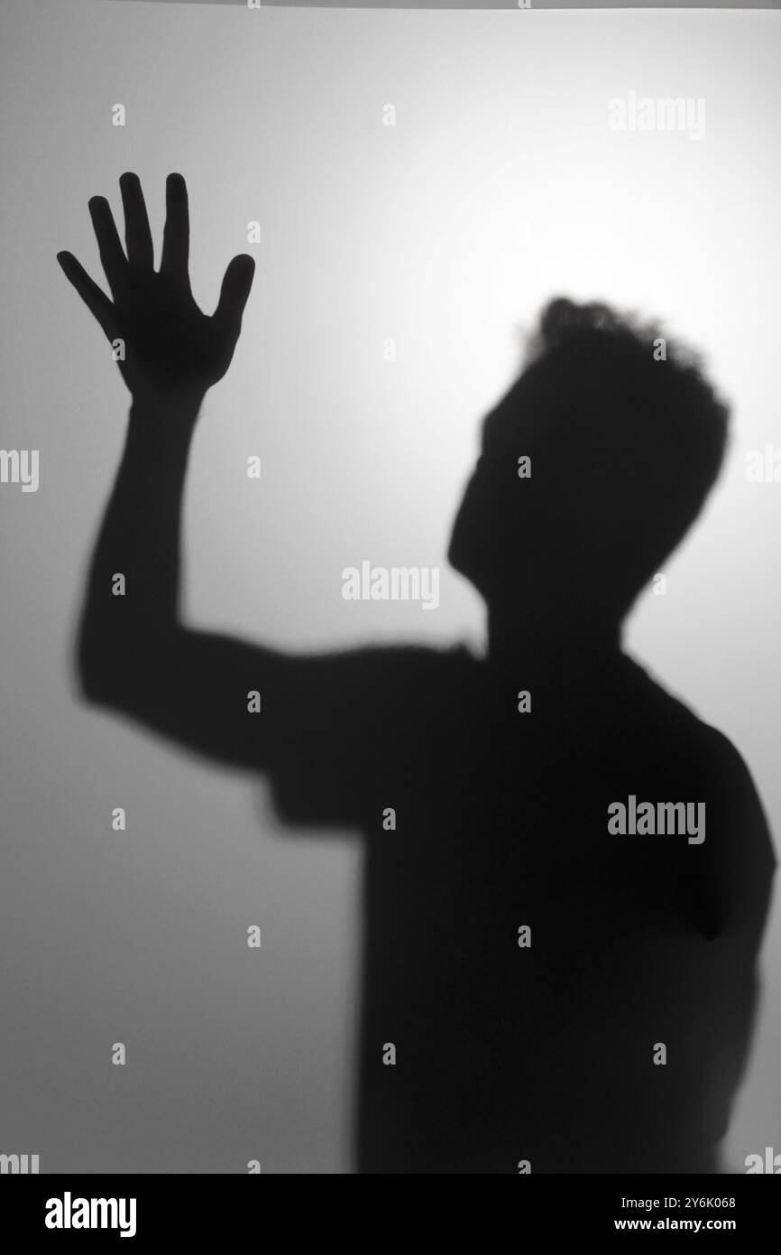 Silhouette eines Mannes, der seine Hand vor einem weißen Hintergrund hebt, abstrakte Fotografie mit hohem Kontrast und Schattenspiel Stockfoto