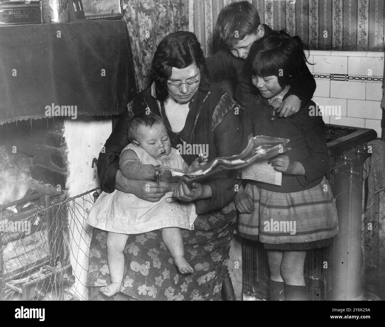 Frau Livesey mit ihrem Baby, das die Nachricht liest, dass der Prinz von Wales Edward VIII. Ihre anderen Kinder zu Hause am 16. März 1932 besucht Stockfoto