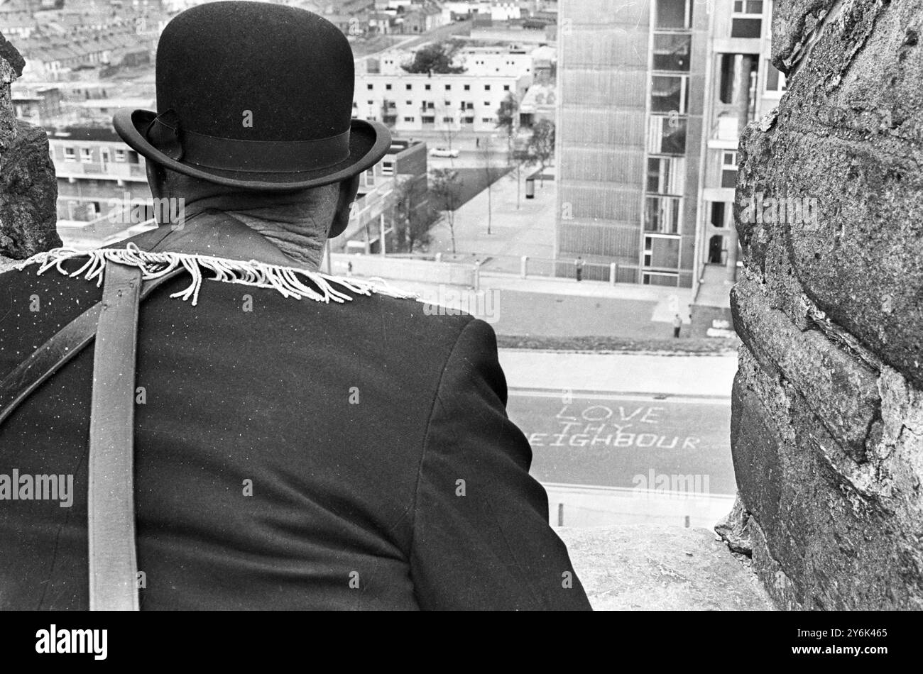 Die römisch-katholische Gegend von Bogside, Londonderry, in dieser unruhigen Stadt sieht ruhig aus, während einer der Orangemen, die am heutigen marsch teilnehmen, den Blick von den alten Stadtmauern aus genießt. Auf die Straße gemalt ist eine Friedensbotschaft " Love Dy Neighbour ". August 1969 Stockfoto