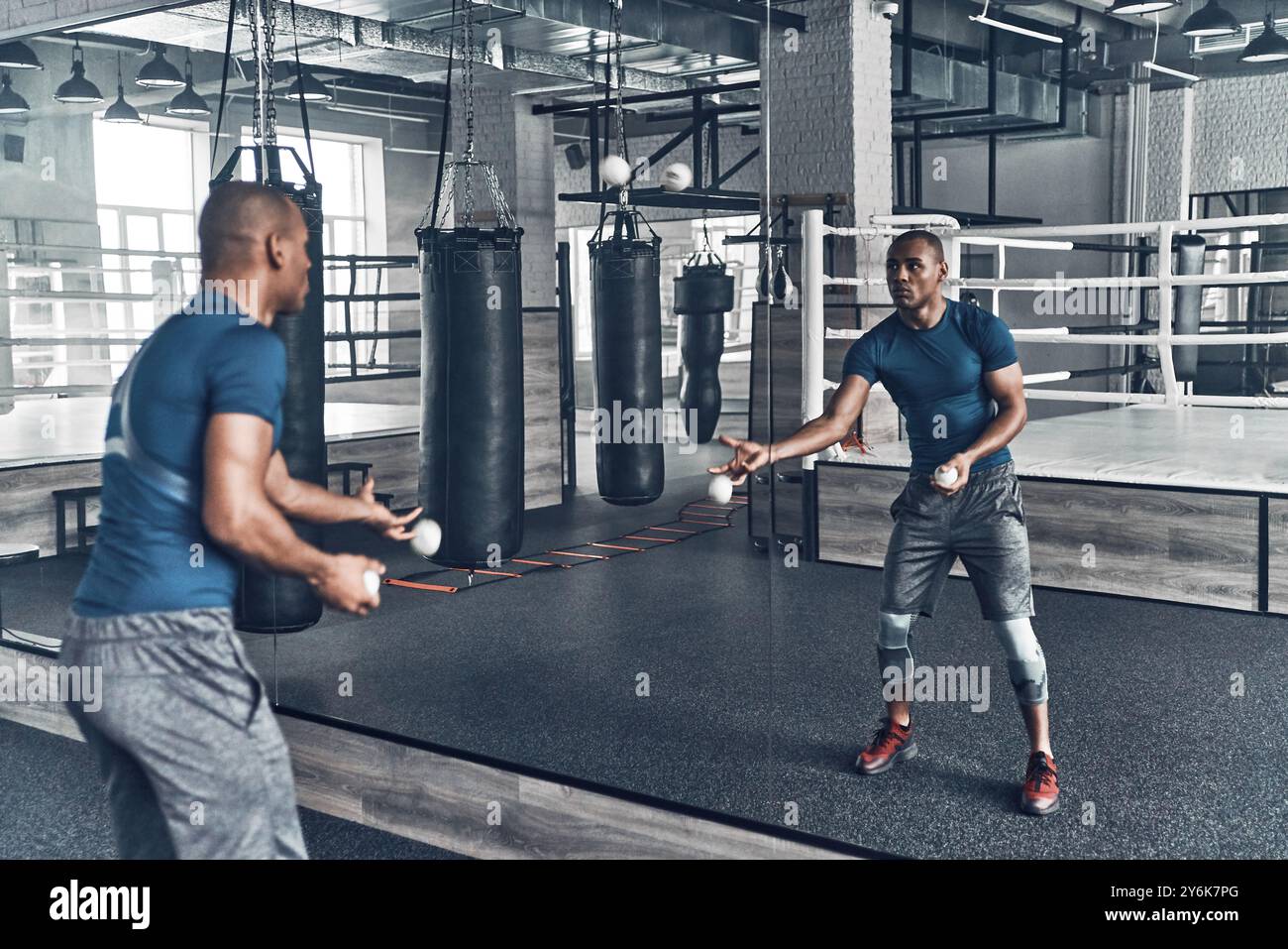 Eine andere Art des Trainings. Hübscher junger afrikanischer Mann in Sportkleidung, der mit Bällen trainiert, während er vor dem Spiegel im Fitnessstudio steht Stockfoto