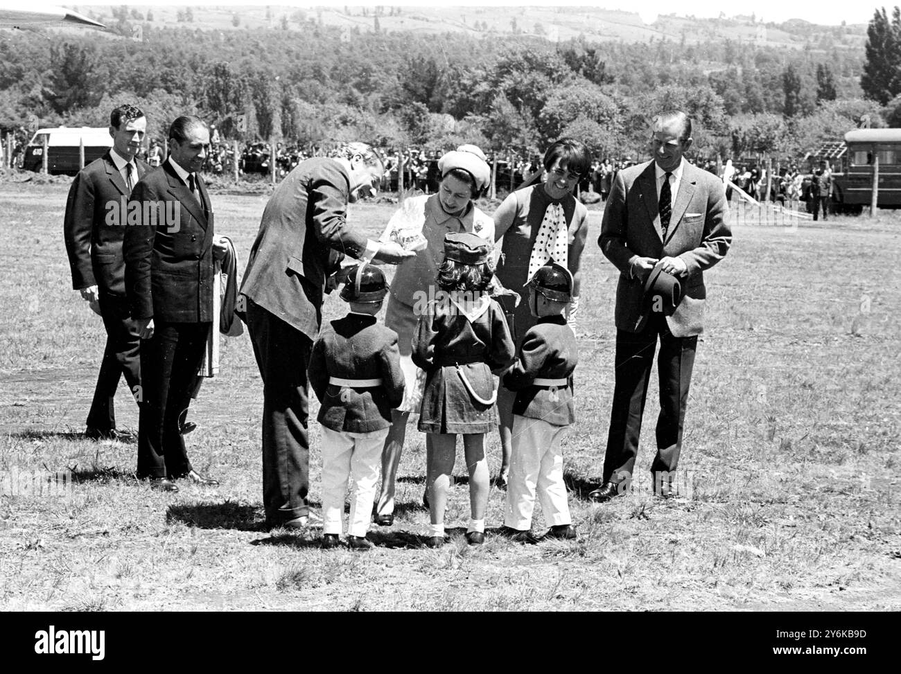 Pucon, Chile: Drei einheimische Kinder (zwei Jungen und ein Mädchen), kleidet sich als Feuerwehrmaskottchen und schenken Königin Elisabeth II. Hier am 15. November einen Blumenstrauß. Den Blumenstrauß der Kinder nimmt Außenminister Valdes. Die Königin in Begleitung von Prinz Philip (ganz rechts) ist auf einem 8-tägigen Staatsbesuch in Chile. 19. November 1968 Stockfoto