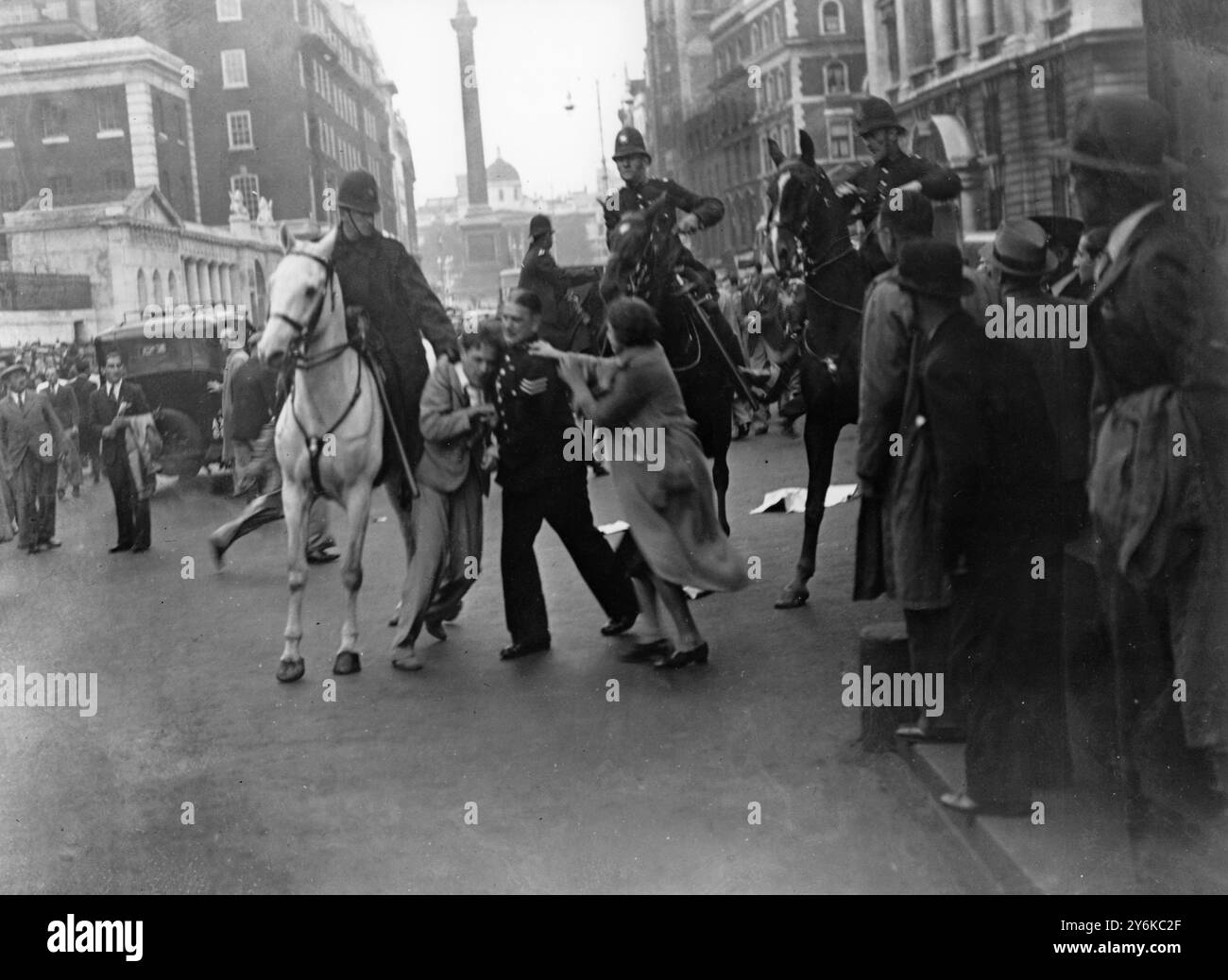 Nach der Friedensdemonstration am Trafalgar Square brachen in Whitehall Unruhen aus, als Mitglieder der Menge versuchten, die Polizeikette zur Downing Street zu brechen. Berg- und Fußpolizisten haben die Menschenmassen wiederholt angegriffen. Foto zeigt: Ein Polizist kämpft mit einem verhafteten Aufständischen in Whitehall, als ein Mädchen eine Rettung versucht. Zwei berittene Offiziere sind dabei, und der linke hat den kämpfenden Mann am Kragen. 8. September 1938 Stockfoto