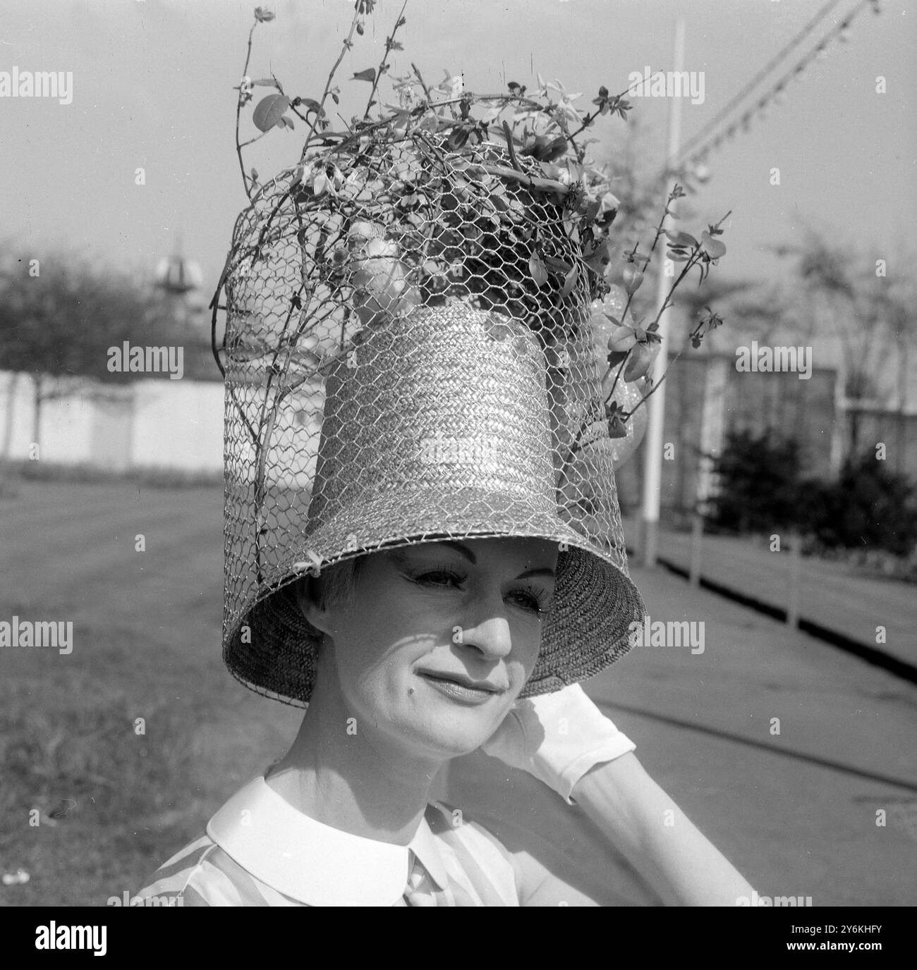 London: Im Bild der Osterparade im Londoner Battersea Park heute Nachmittag ist Mrs. Irene Masure aus Hampstead zu sehen, die ihren Wellensittich "Billy Boy" in einem vergoldeten Käfig für ihre Ostermütze nutzte Glücklicherweise kam auch die Frühlingssonne heraus und machte so einen fröhlichen Osterausflug für Mrs. Masure und ihr Haustier. - 22. April 1962 Stockfoto