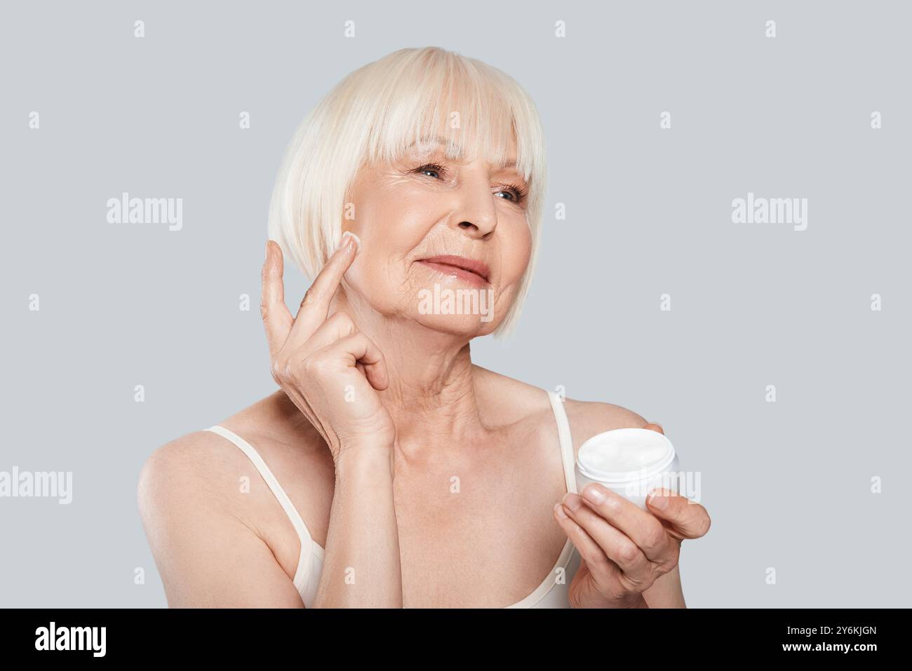 Fühlt sich gut an... Schöne Seniorin, die Kosmetikprodukte anwendet, während sie vor grauem Hintergrund steht Stockfoto