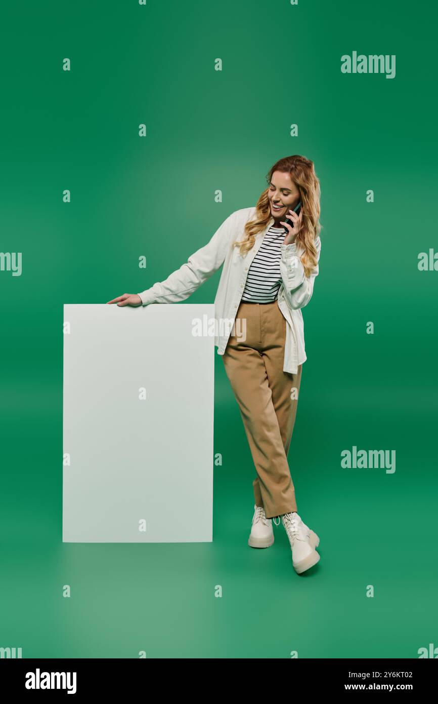 Eine schöne Frau mit lockigem Haar genießt ein Telefongespräch, während sie sich lässig gegen eine leere Oberfläche lehnt. Stockfoto