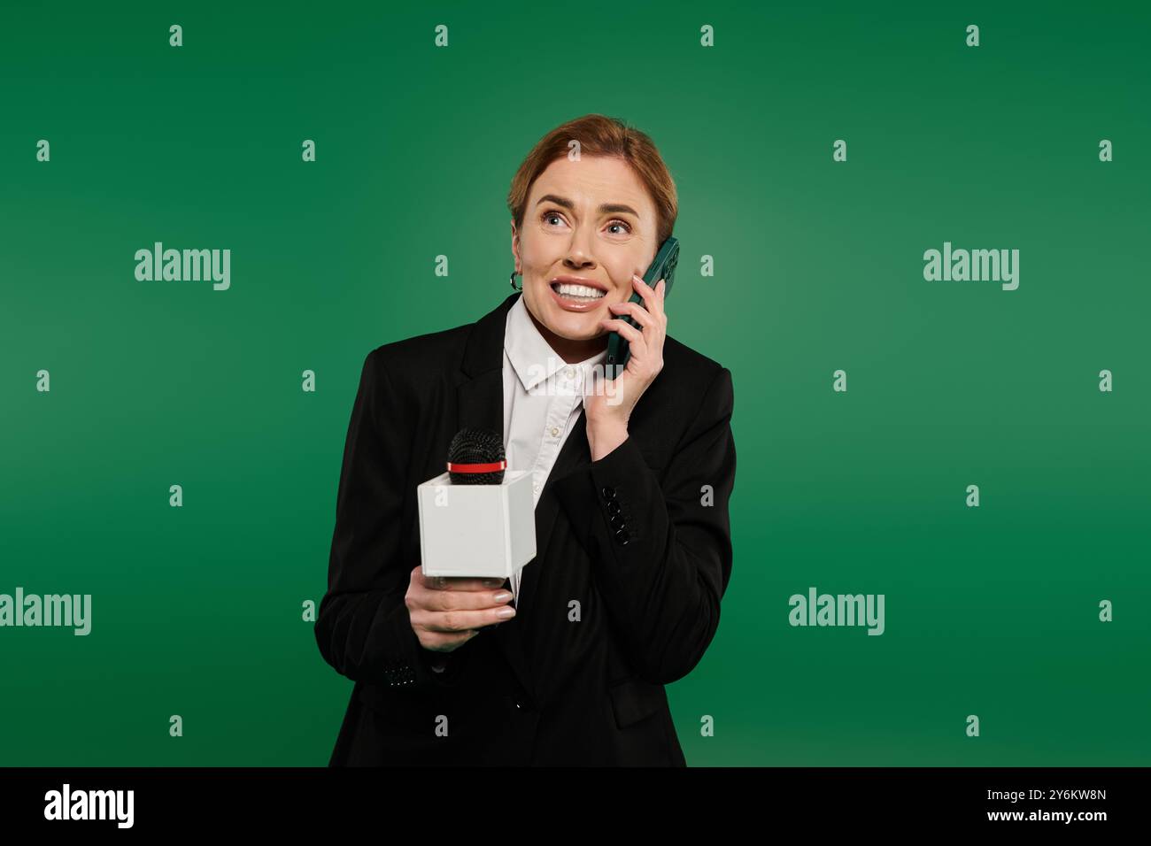 Ein Fernsehmoderator in formellen schwarzen Chats am Telefon vor grüner Kulisse begeistert. Stockfoto