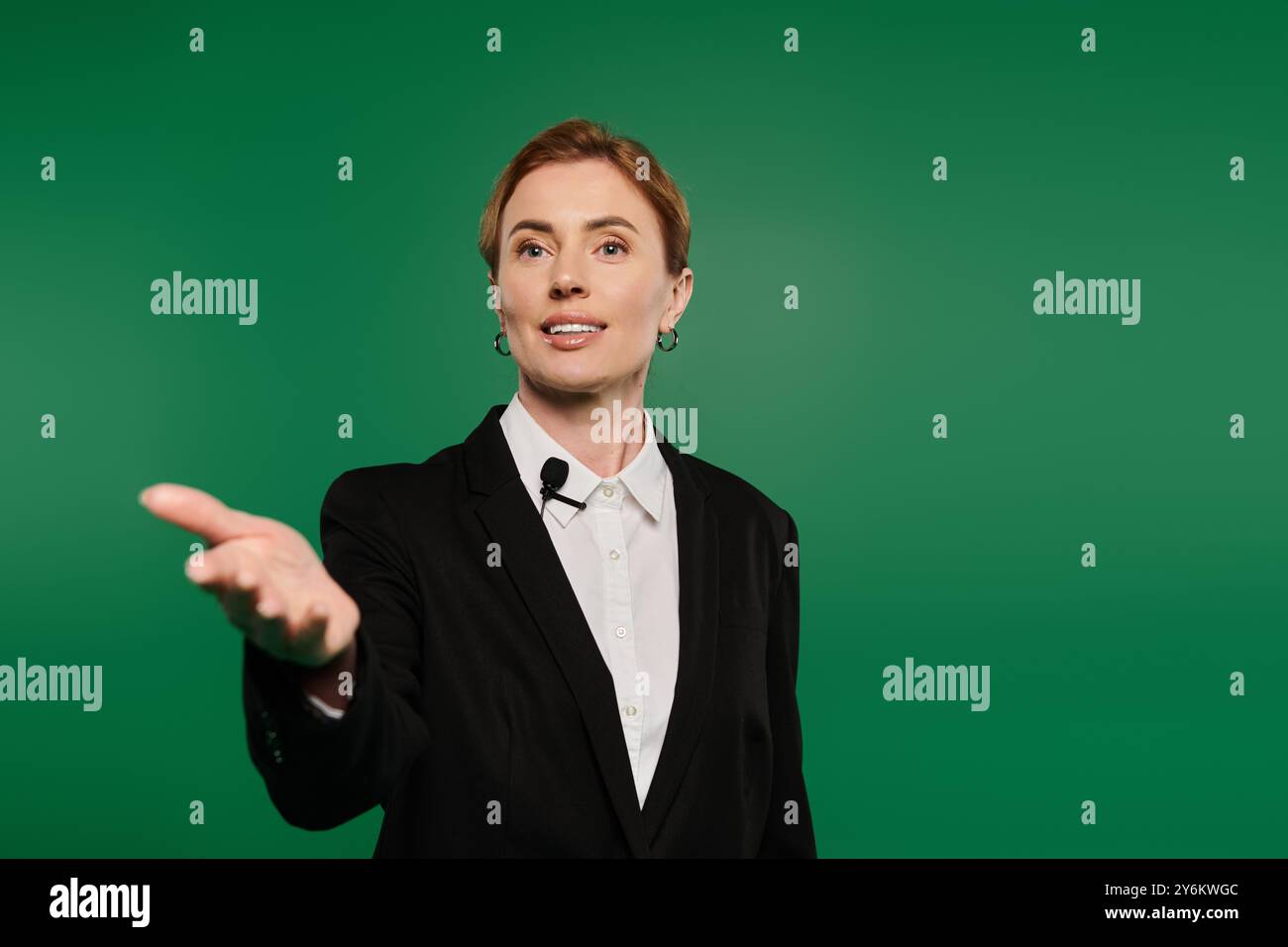 Ein zielstrebiger Fernsehmoderator in formeller schwarzer Kleidung fesselt das Publikum vor einem leuchtend grünen Hintergrund. Stockfoto