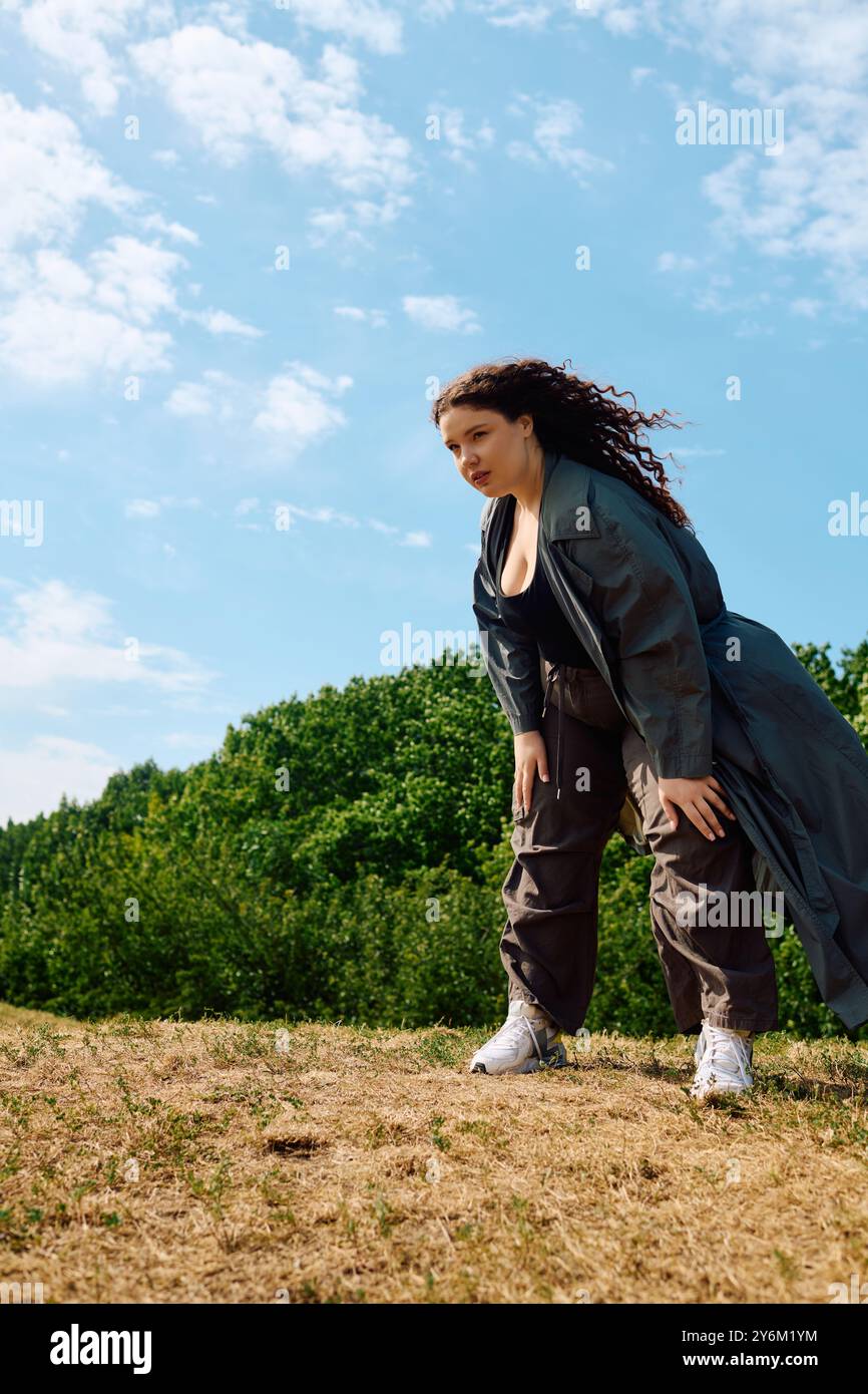 Eine freudige Frau in Übergröße beugt sich auf einem grasbewachsenen Feld und nimmt die Schönheit der Natur um sie herum wahr. Stockfoto