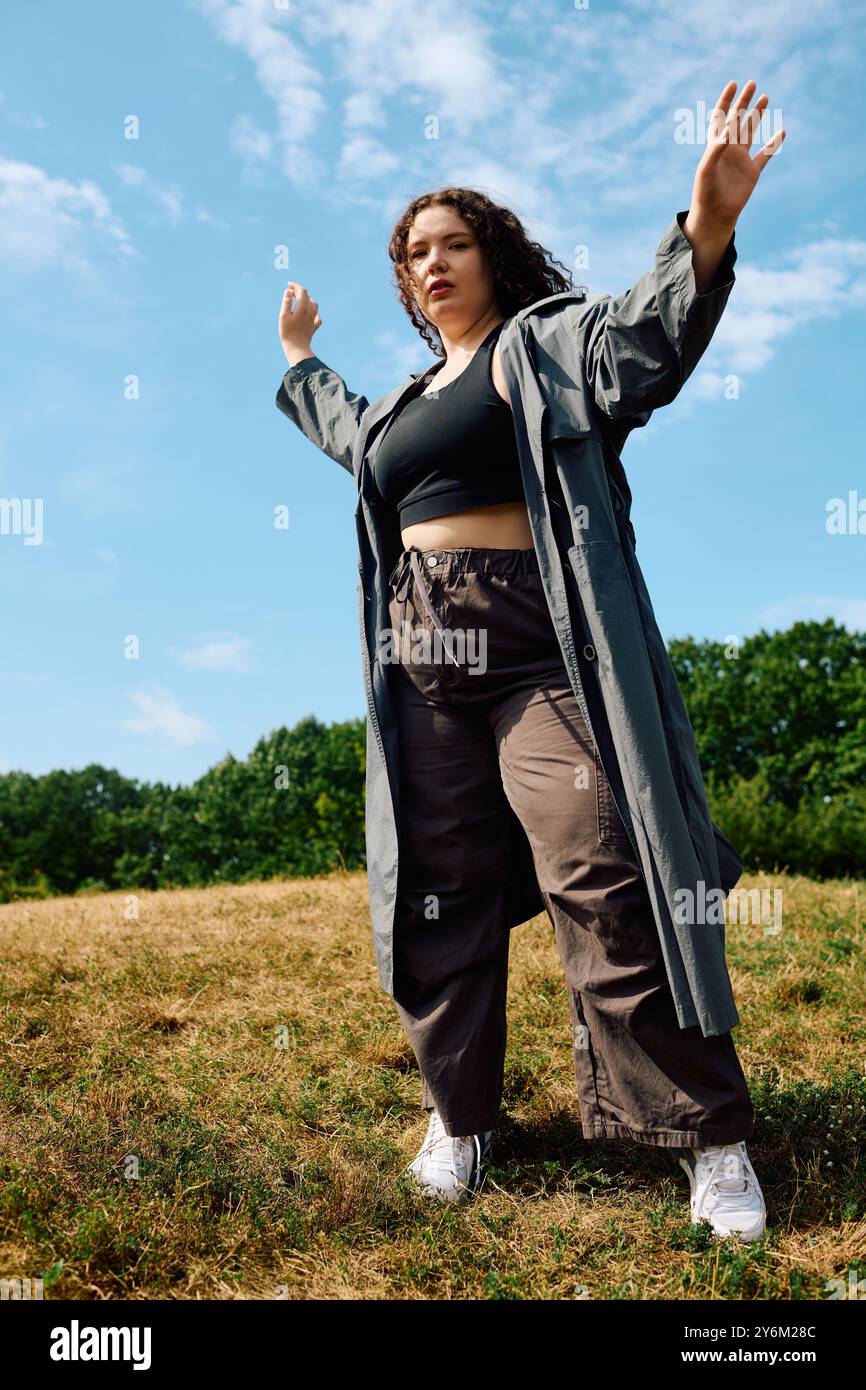 Eine Frau in Übergröße begrüßt die Freiheit und tanzt fröhlich auf einem lebendigen, sonnendurchfluteten Feld unter dem blauen Himmel. Stockfoto