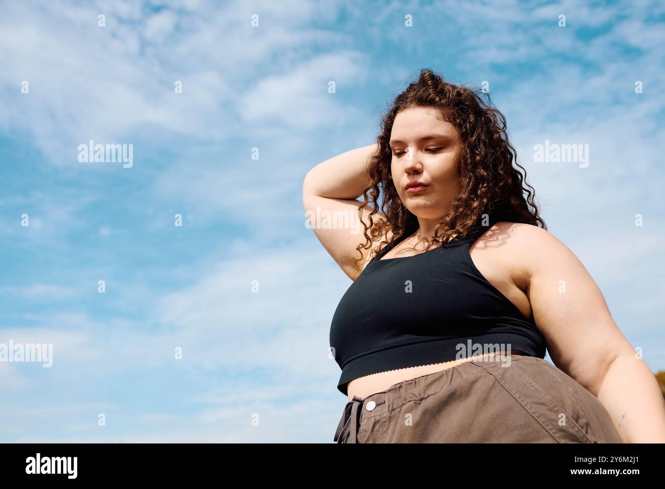 Eine selbstbewusste Frau in Übergröße steht anmutig auf einem üppigen, offenen Feld und sonnt sich im Sonnenlicht. Stockfoto