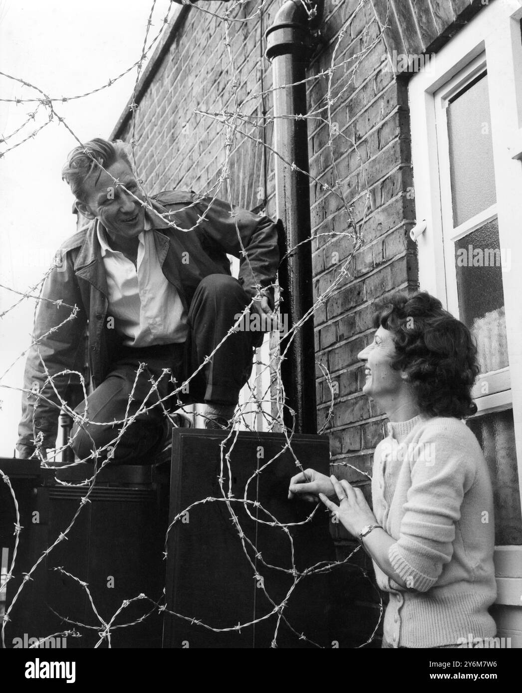 Der Ex-Fallschirmjäger Donald Cook, 38 Jahre alter Flugzeuginspektor und Sekretär der St. Pancras United Pächtervereinigung, spricht mit seiner 36 Jahre alten Frau Edith durch eine Barriere aus Stacheldraht und zwei umgedrehten alten Klavieren in ihrer Wohnung im obersten Stockwerk des Kennistoun House, einem Block der St. Pancras Council-Wohnungen in der Leighton Road, Kentish Town, London. Eine Räumungsmeldung, die Mr. Cook serviert wird, läuft um Mitternacht ab und er sagt, er sei bereit, wenn nötig, auf eine dreijährige Belagerung. Eine Rakete wird abgefeuert, als Zeichen, dass die Gerichtsvollzieher angekommen sind Mr. Cook, Vater von vier Kindern, sagte, er schulde etwa 56 Pfund in r Stockfoto