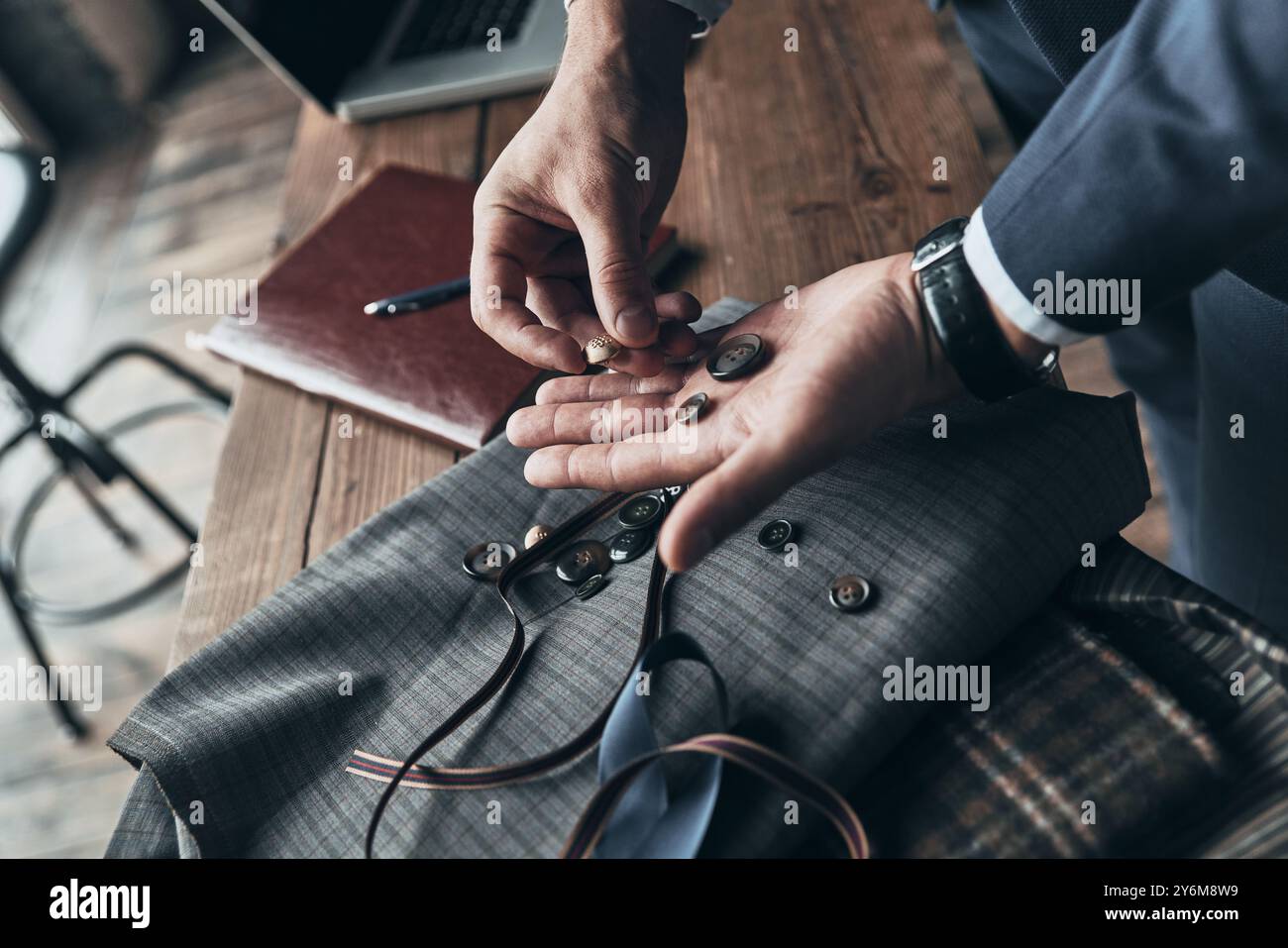 Suche nach der richtigen Entscheidung. Nahaufnahme des Modedesigners, der während seiner Arbeit im Modestudio Knöpfe auswählt Stockfoto