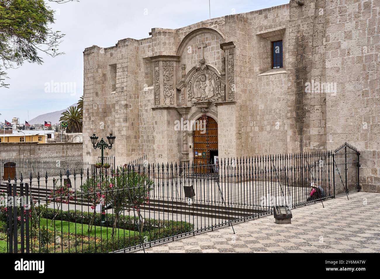 Wunderschöner Blick auf einen historischen Klostereingang in Arequipa, Peru. Die Szene zeigt komplizierte Steinschnitzereien, eine Holztür und dekorative Gärten Stockfoto